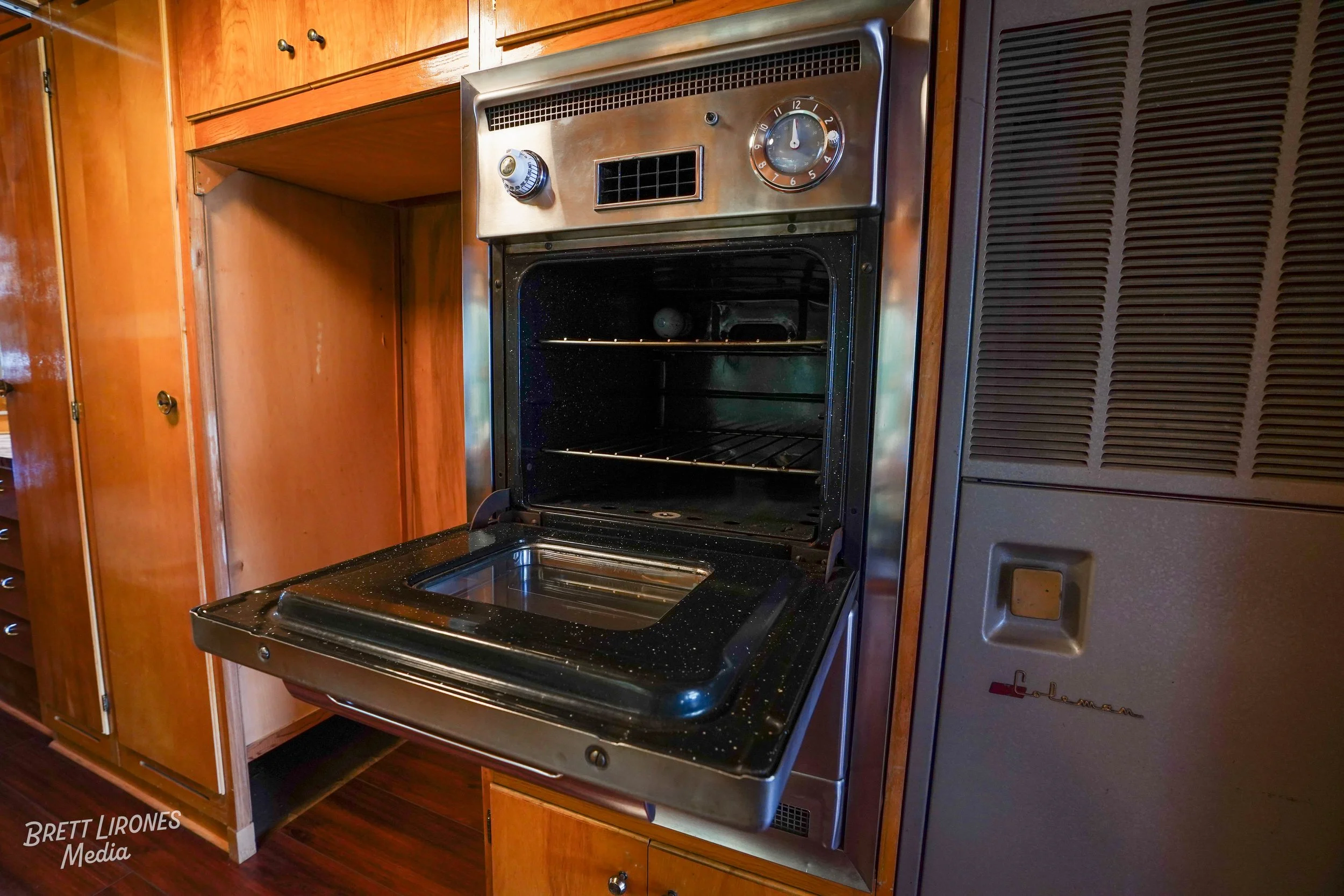 Open vintage black and stainless steel oven with a glass window door in a kitchen with wood cabinets.