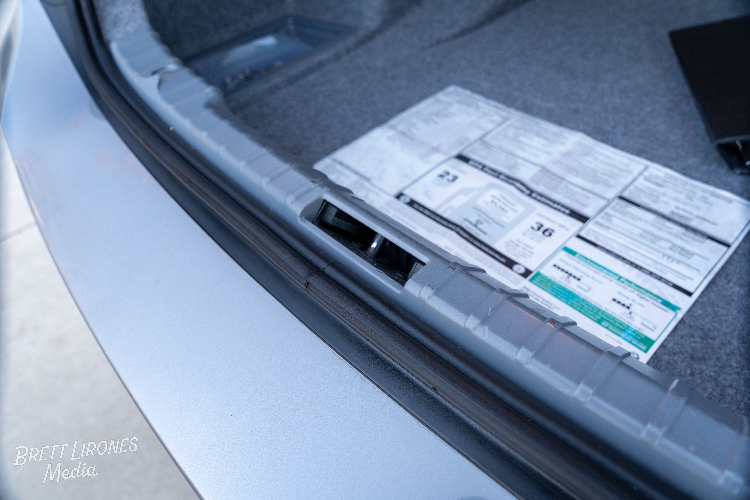 Close-up of a car's trunk showing a sheet of informational stickers or papers under the trunk liner.
