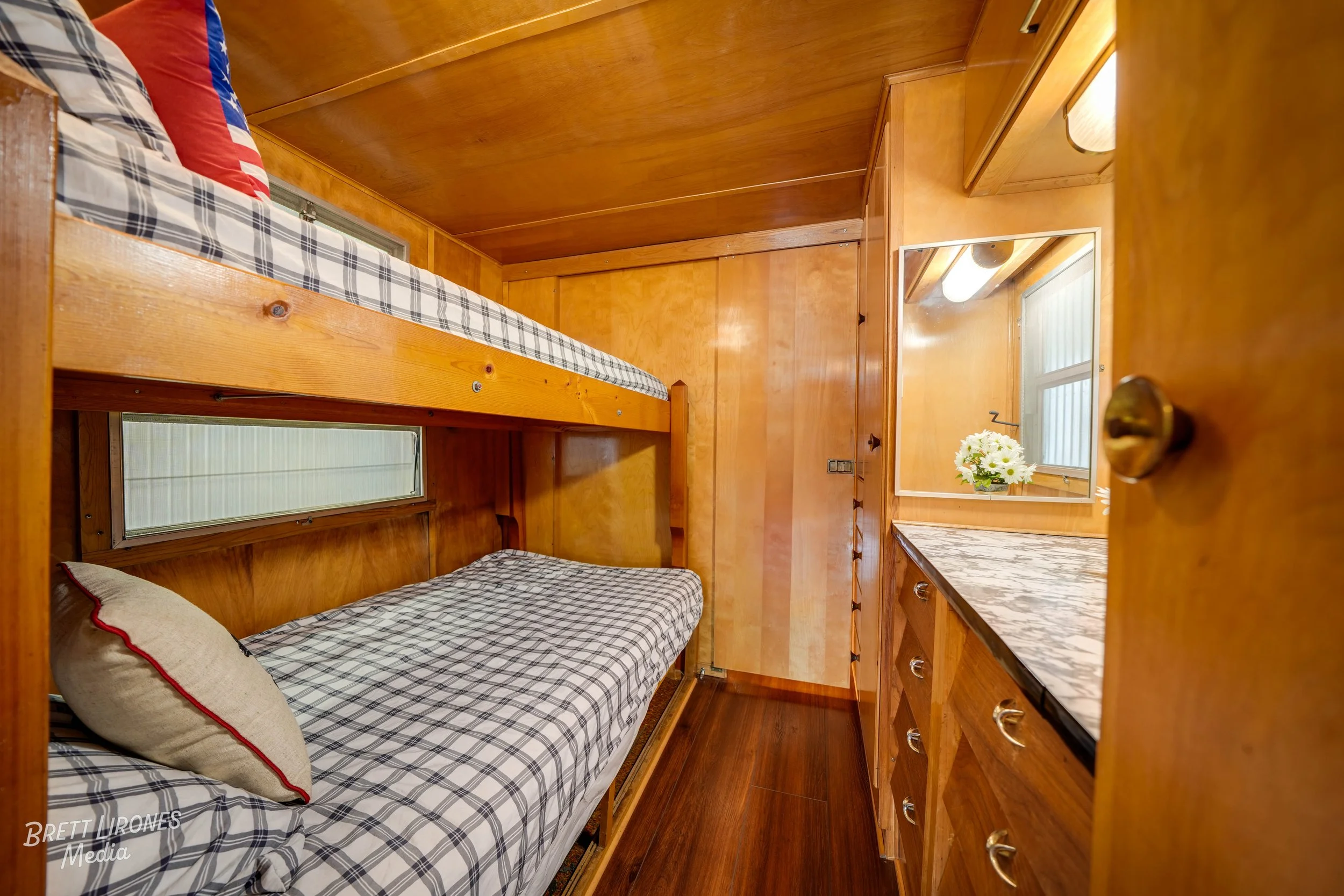Wood-paneled room with bunk beds, a window, a cabinet, a countertop, and a mirror with flowers on it.