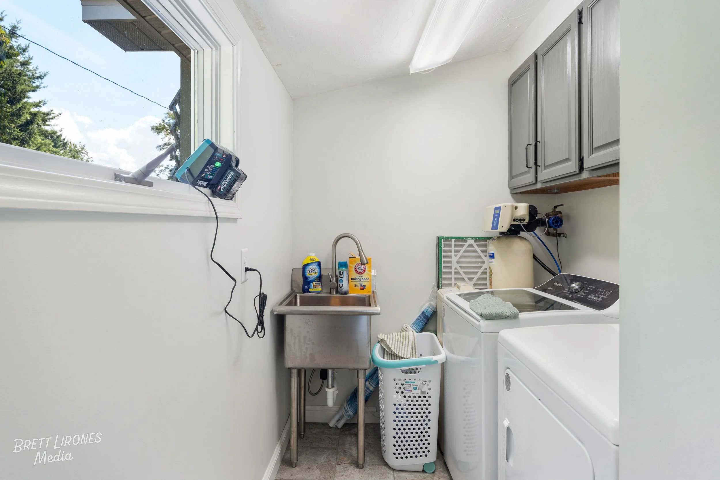 Small laundry room with a window, laundry appliances, sink, and storage cabinets.