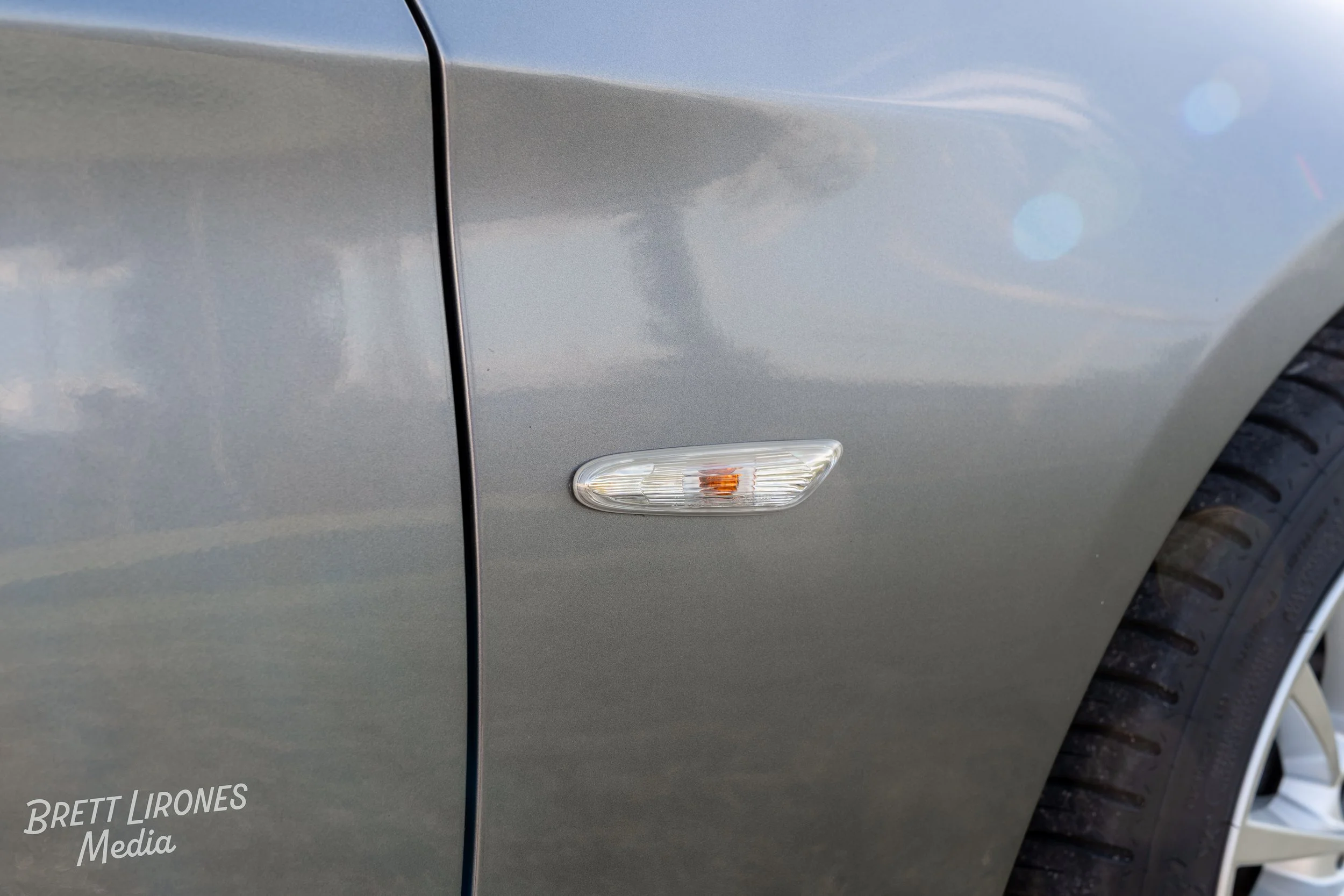 Close-up of a silver car's side, showing a small side marker light and part of the front wheel with tire tread.