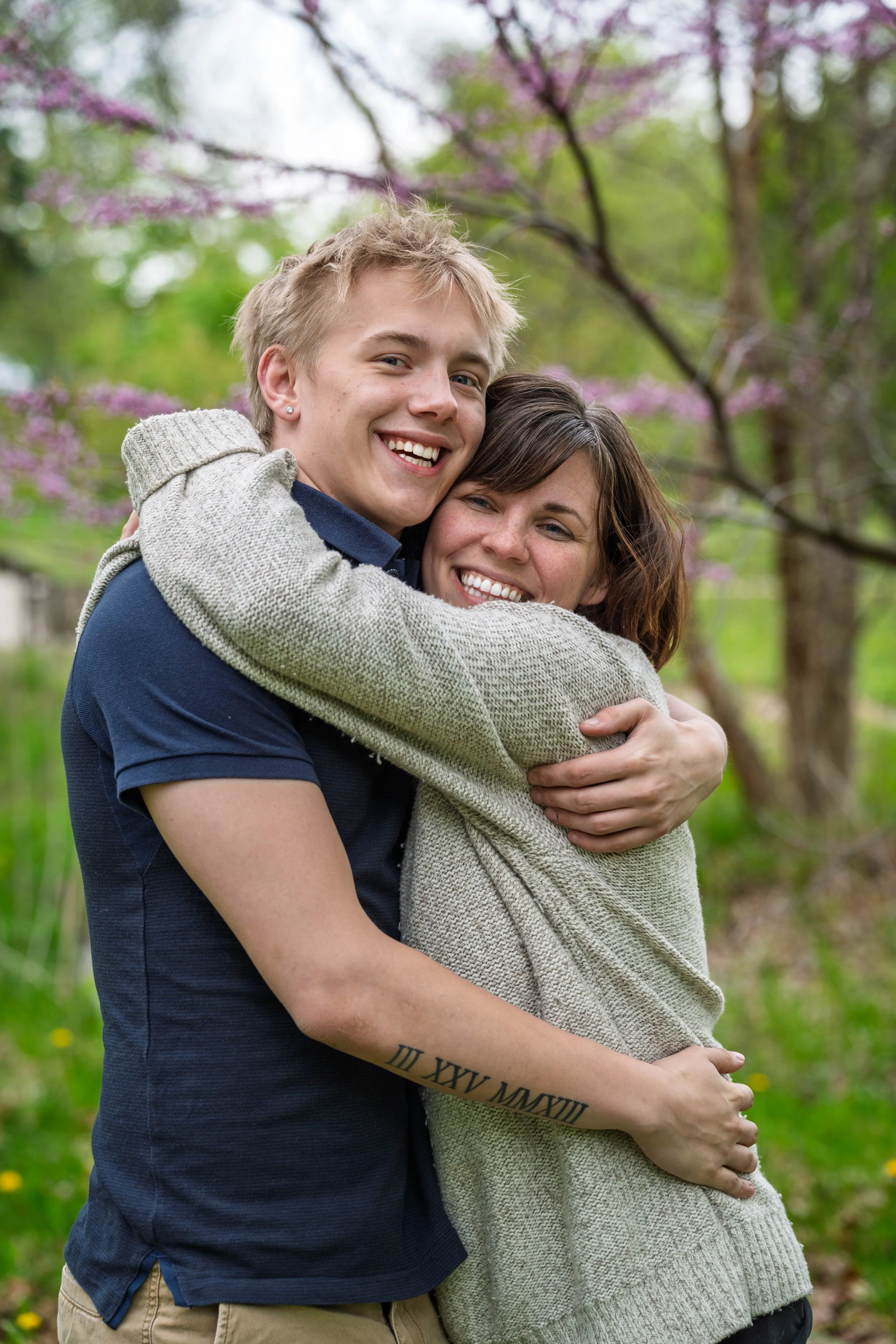 A happy couple hugging outdoors in a park with blooming trees.