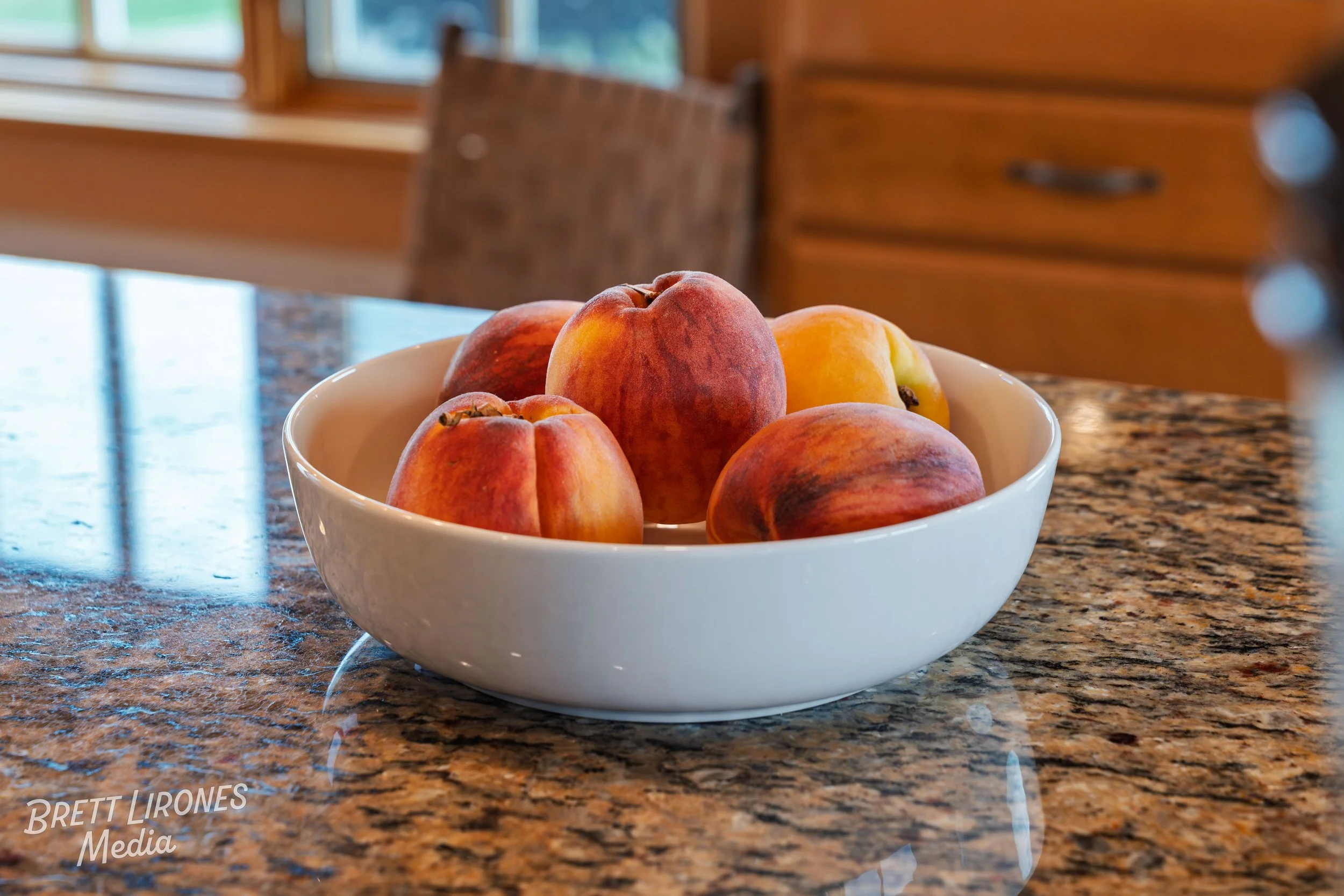 A white bowl filled with peaches and nectarines on a granite countertop in a kitchen.
