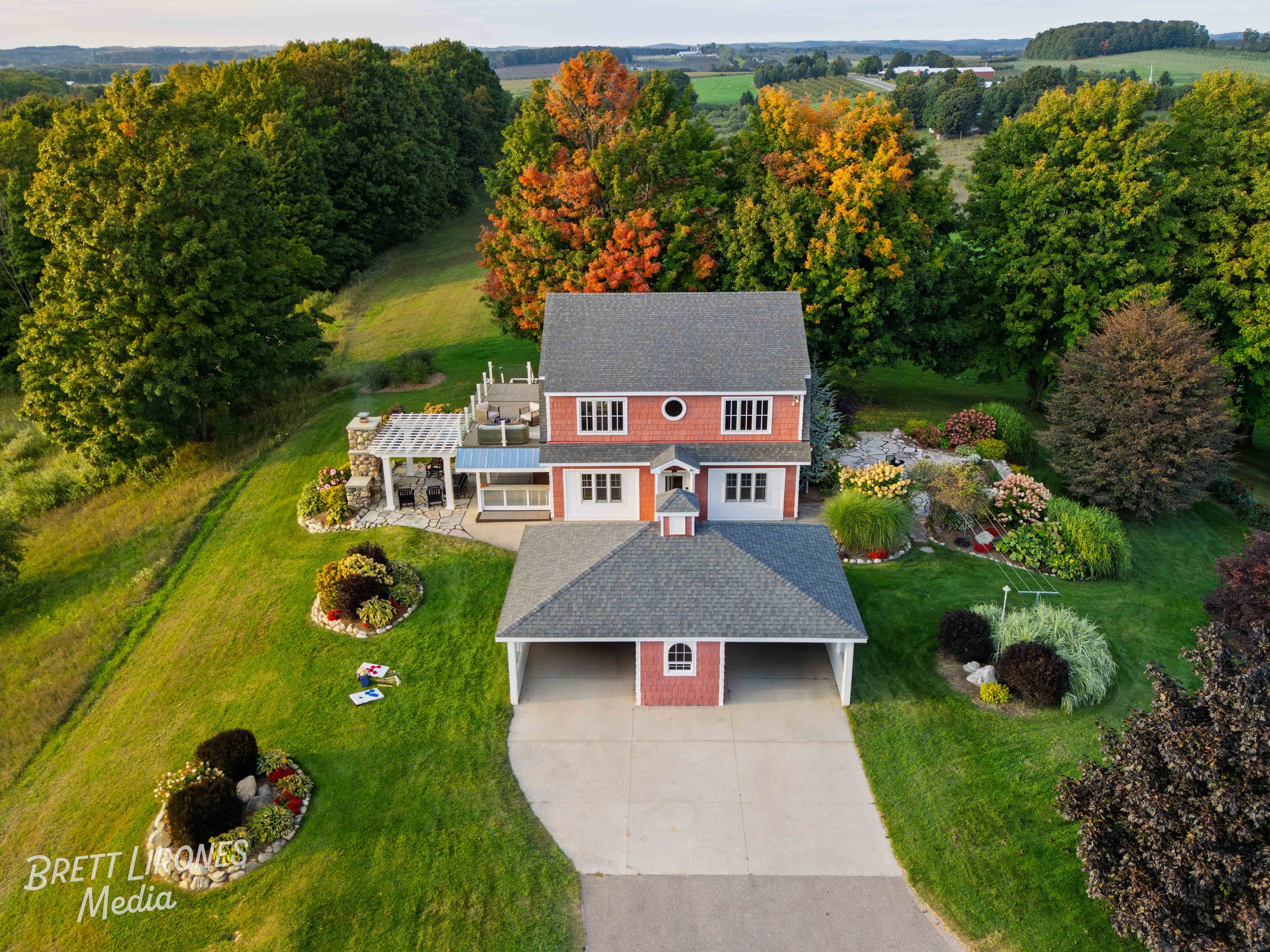 An aerial view of a two-story house with a landscaped yard and garden, surrounded by trees with colorful fall foliage, in a rural countryside setting.
