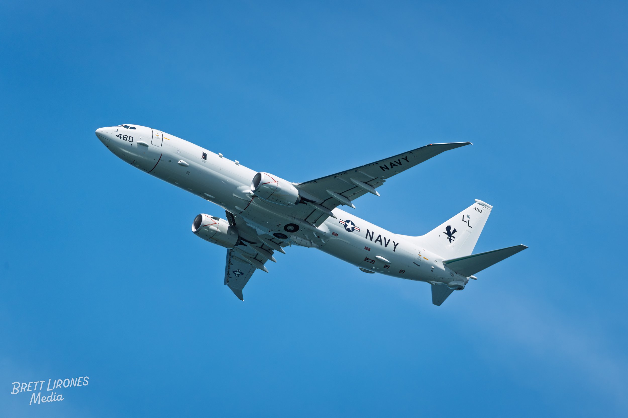 A white United States Navy aircraft flying in a clear blue sky with no clouds.