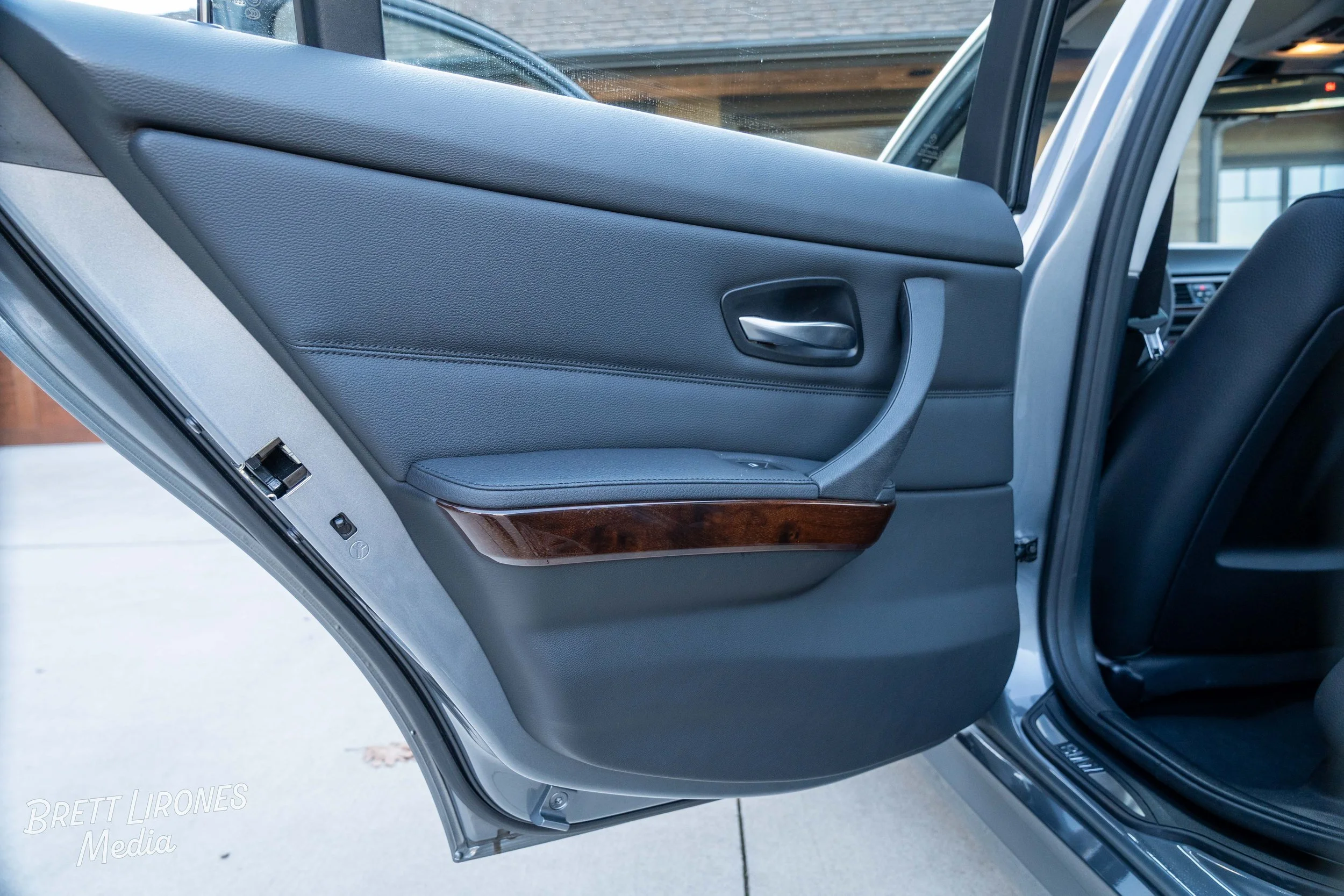 Close-up of a car's interior door panel, featuring a black plastic handle, gray fabric, and a wood trim accent.