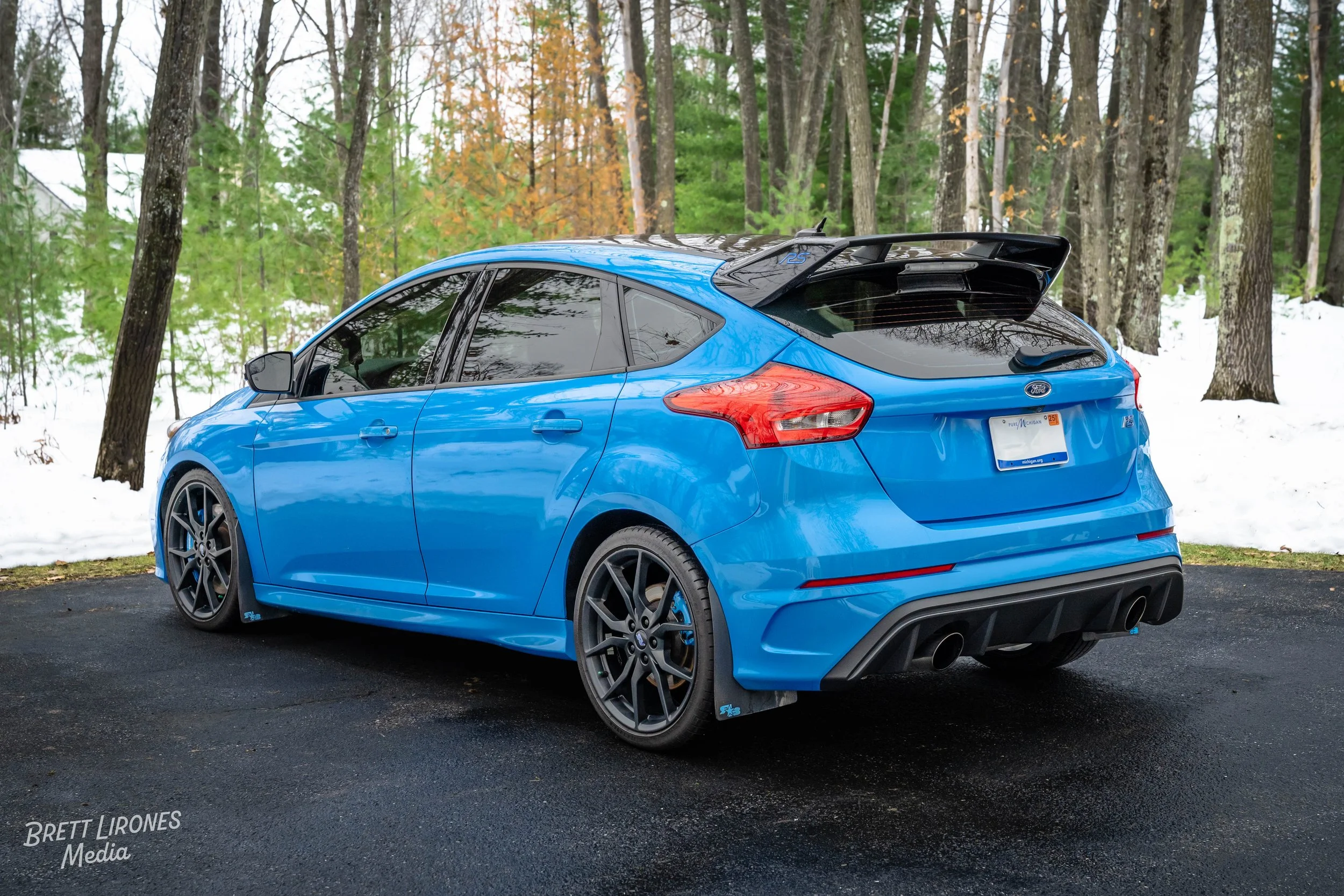 Blue Ford Focus RS parked on asphalt driveway in a wintery wooded area with snow and trees.