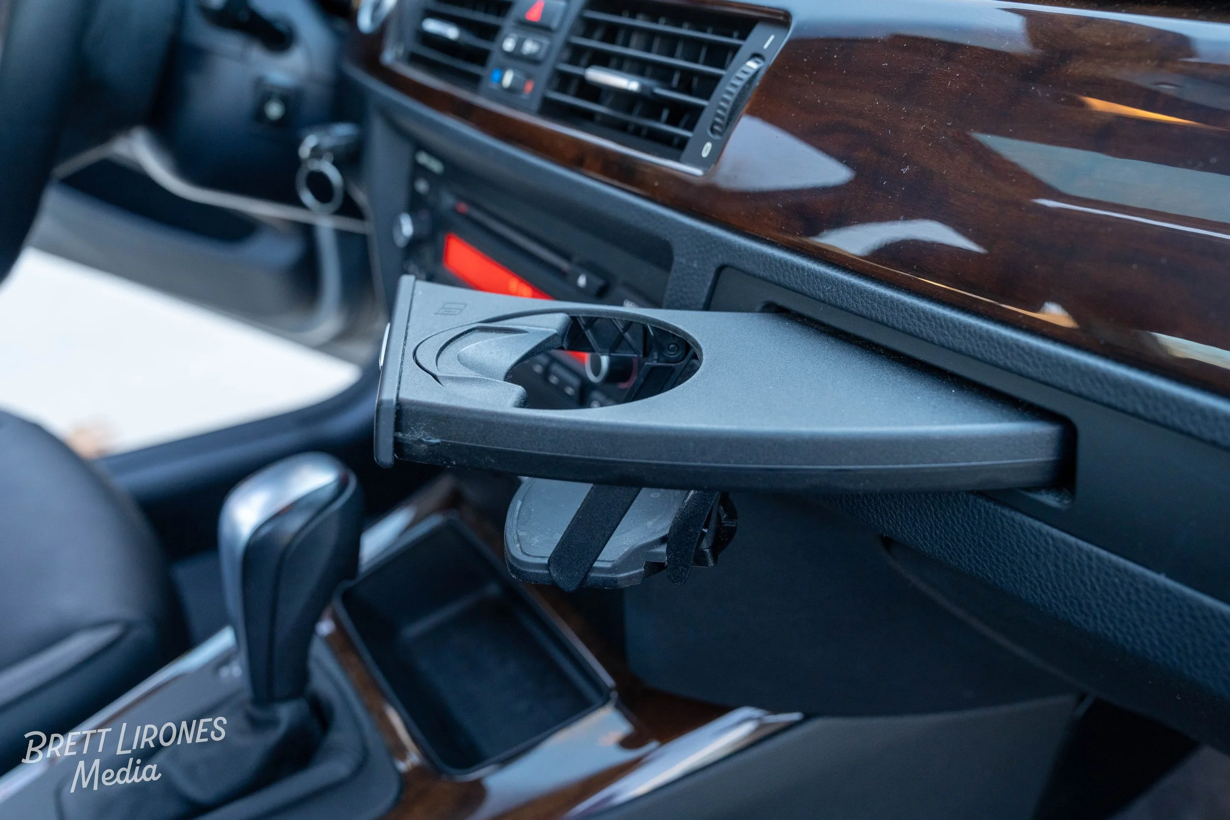 Interior of a car dashboard with a mounted cup holder and gear shift, with wood trim accents.