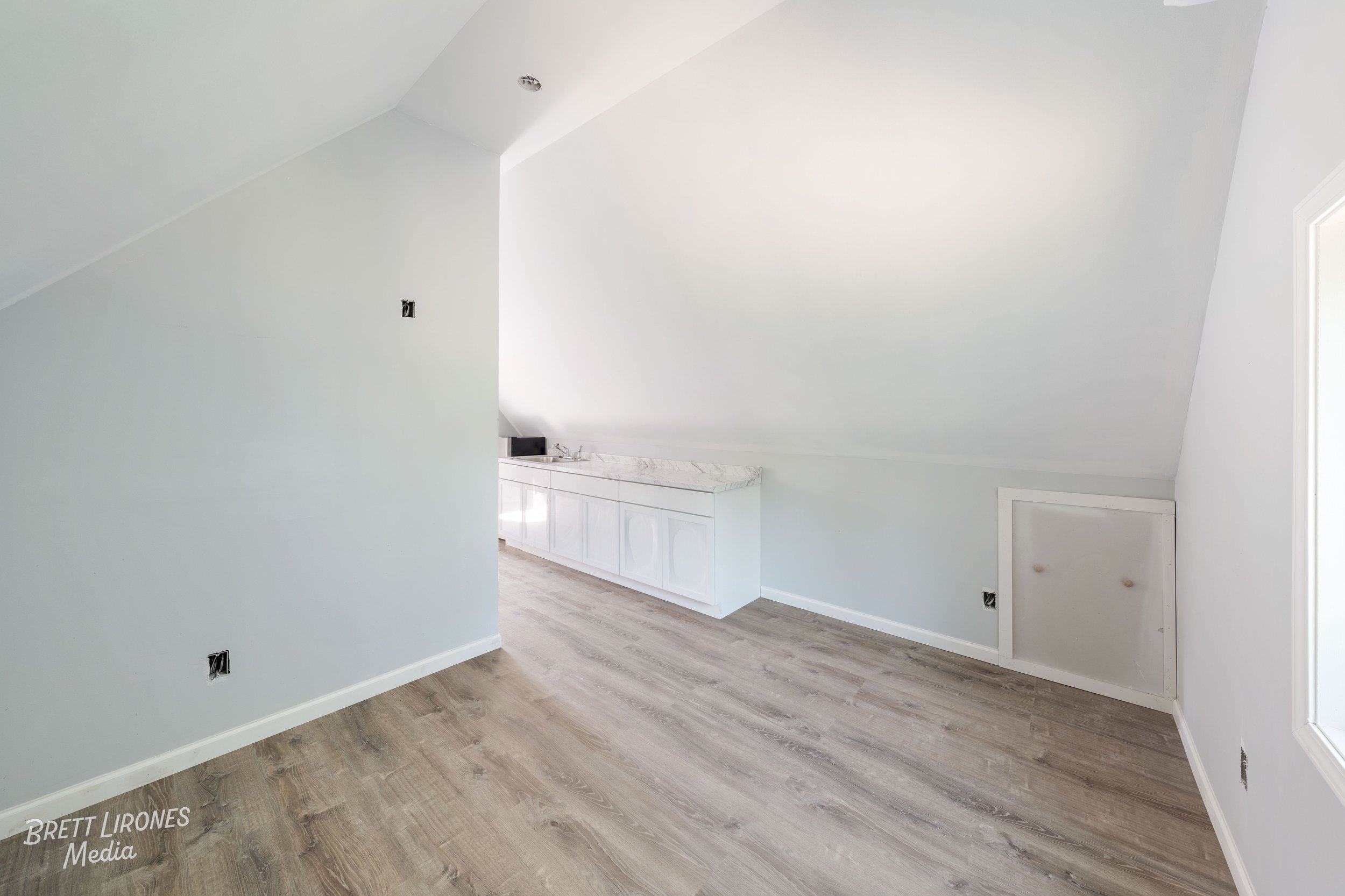 Empty room with white walls, light wood flooring, and a small built-in cabinet door on the right wall.