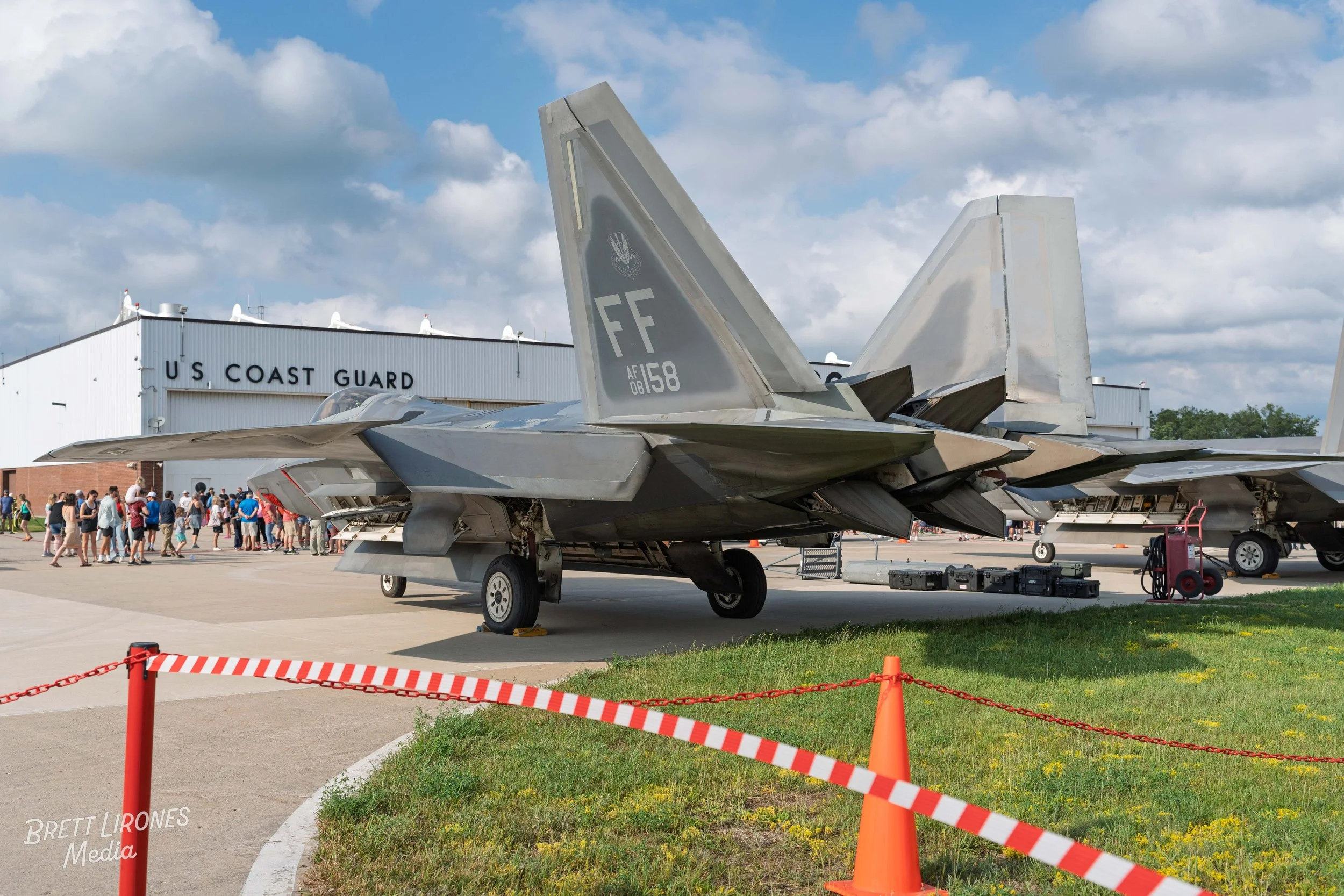 Fighter jet aircraft on display at an airshow, with the U.S. Coast Guard building in the background and a group of people observing.