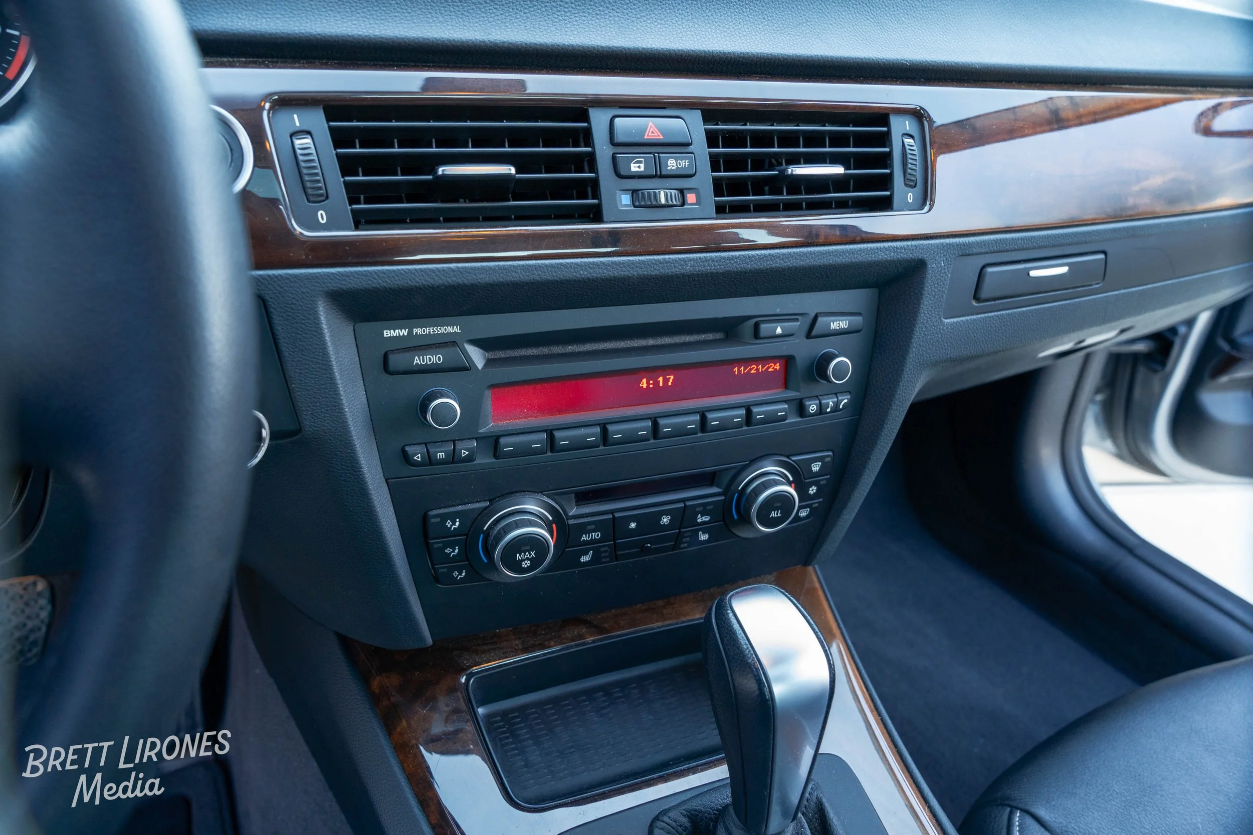 The interior dashboard of a BMW vehicle showing climate control and audio system with a wooden trim.