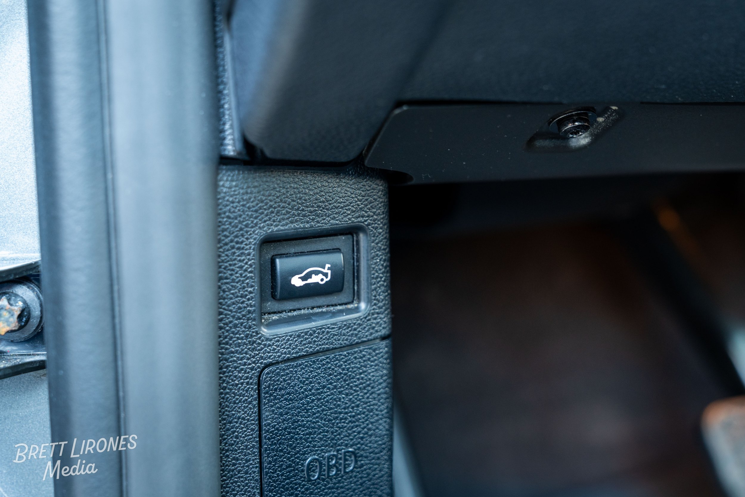 Close-up of a car trunk release button on a black textured dashboard.