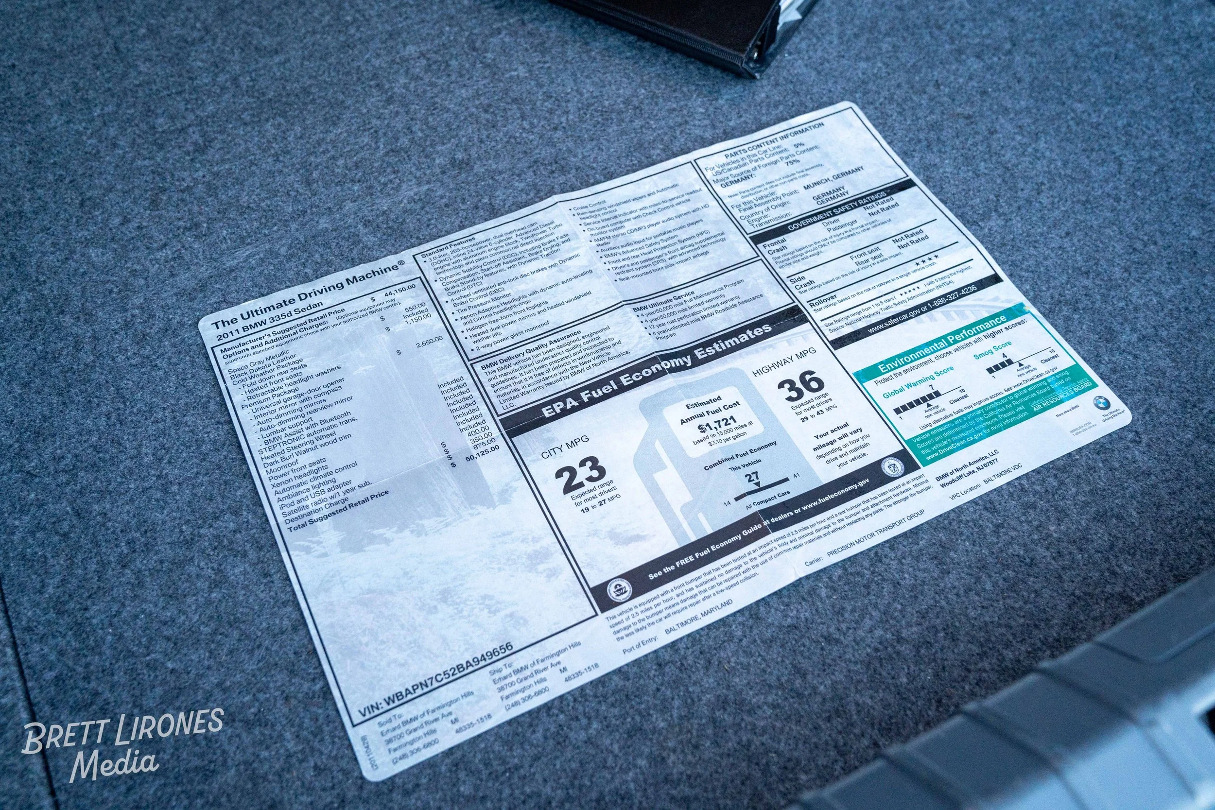 A window sticker for a 2011 BMW 335d Sedan, showing EPA fuel economy estimates, options, and pricing information, placed on a gray surface.