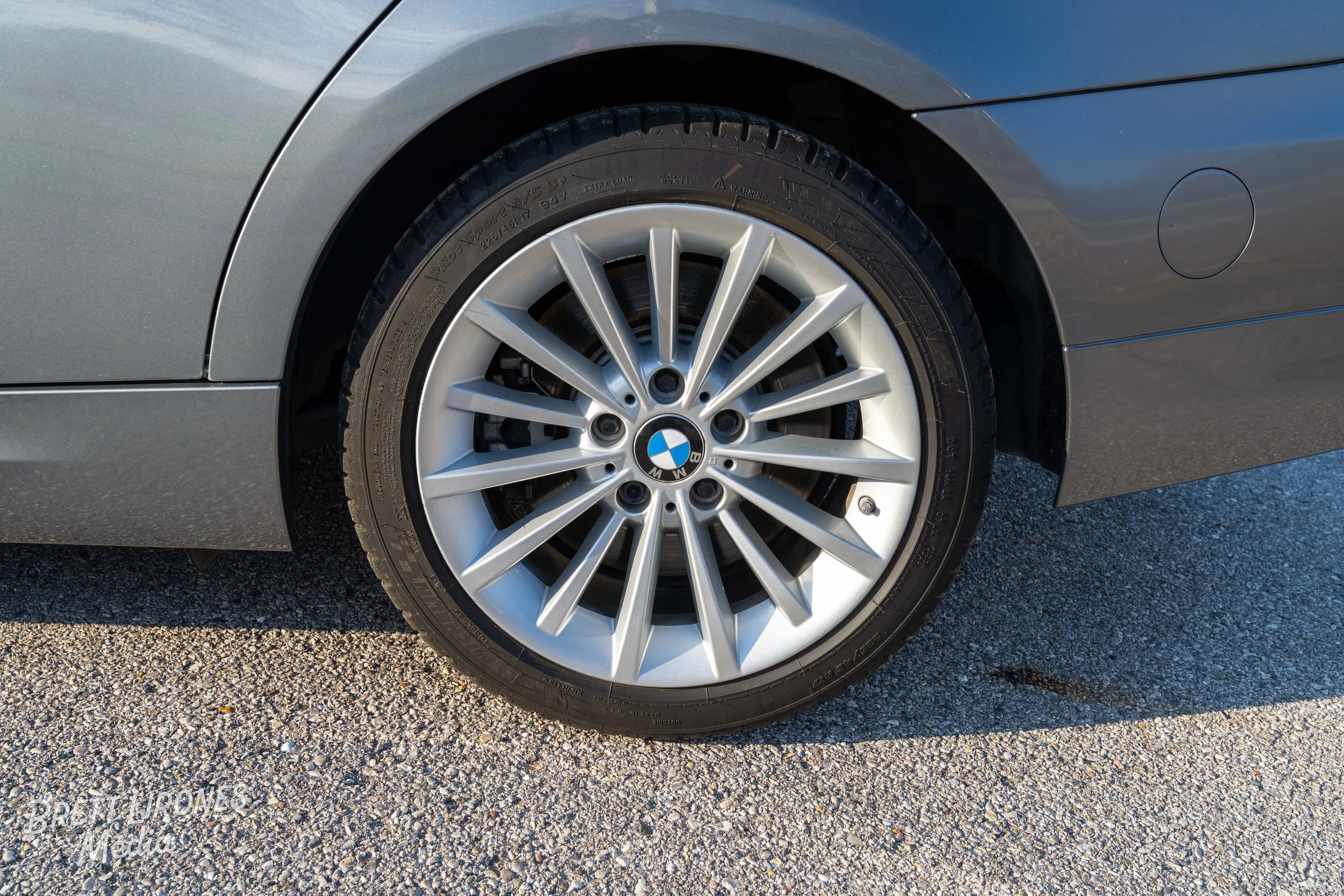 Close-up of a BMW car wheel with silver alloy rim and black tire, parked on gravel.