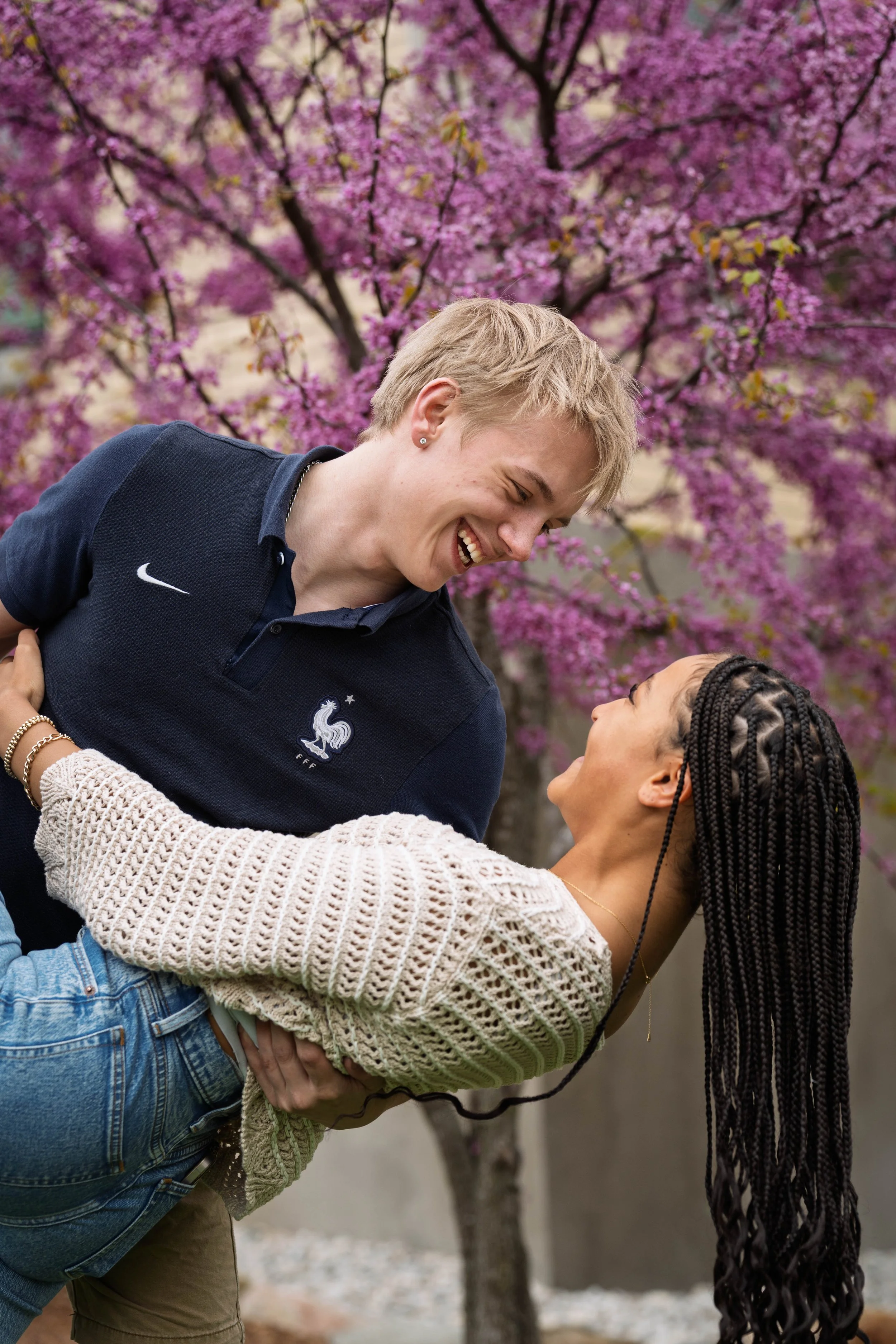A couple dancing outdoors under pink cherry blossom trees, smiling and enjoying each other's company.