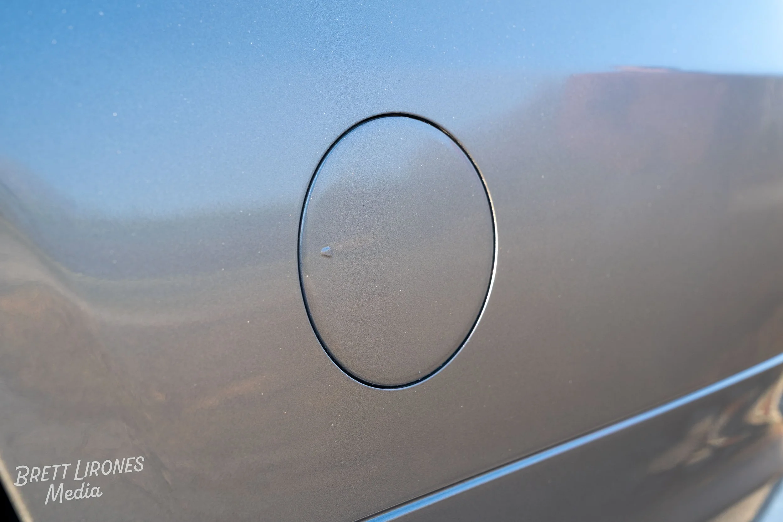 Close-up of a metallic gray vehicle fuel door on a car with a small water droplet nearby.