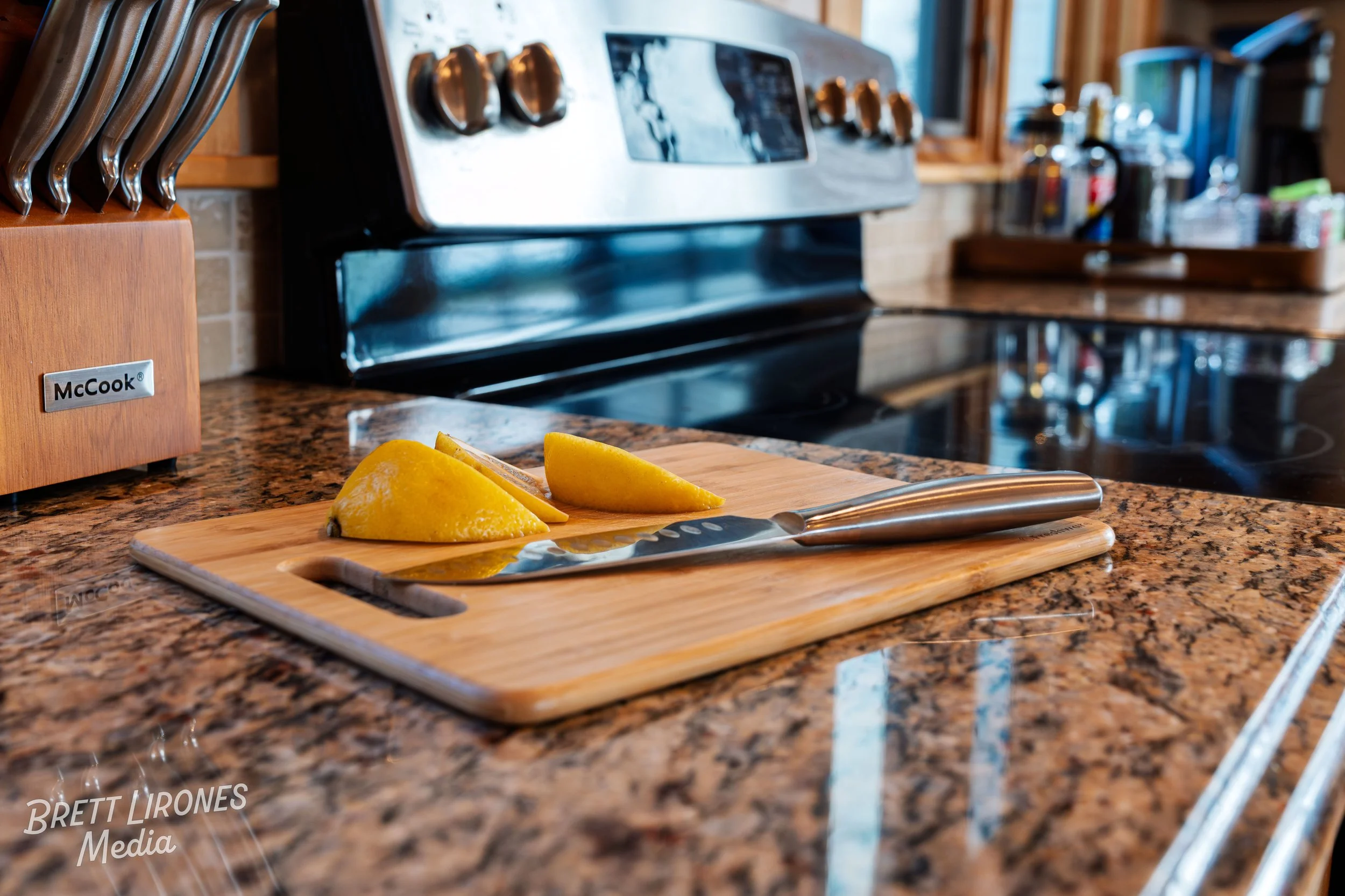 A kitchen countertop with a cutting board, a knife, two lemon halves, a knife block, and a stove in the background.