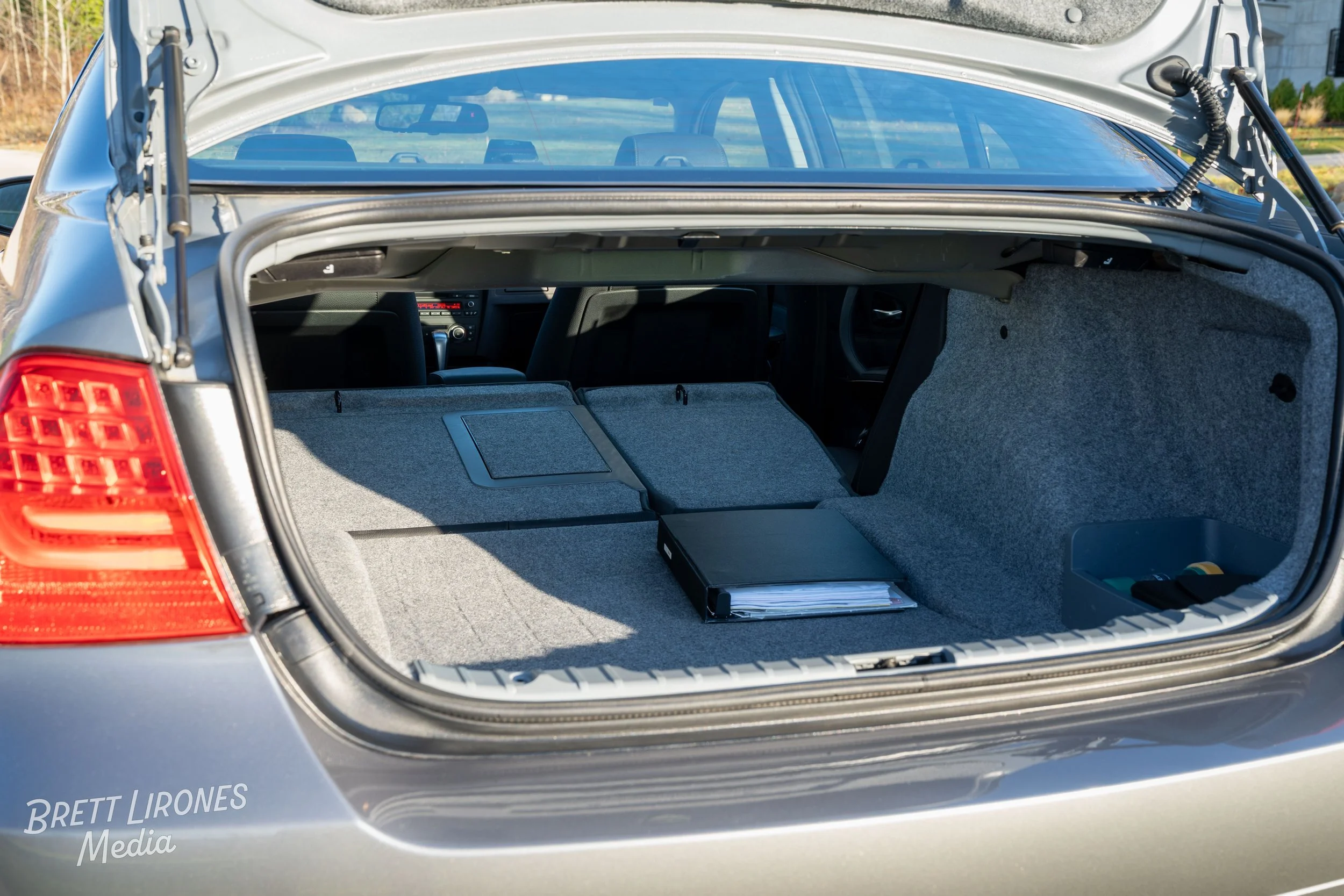 Open trunk of a silver car showing gray carpeted interior with some folders and tools inside.