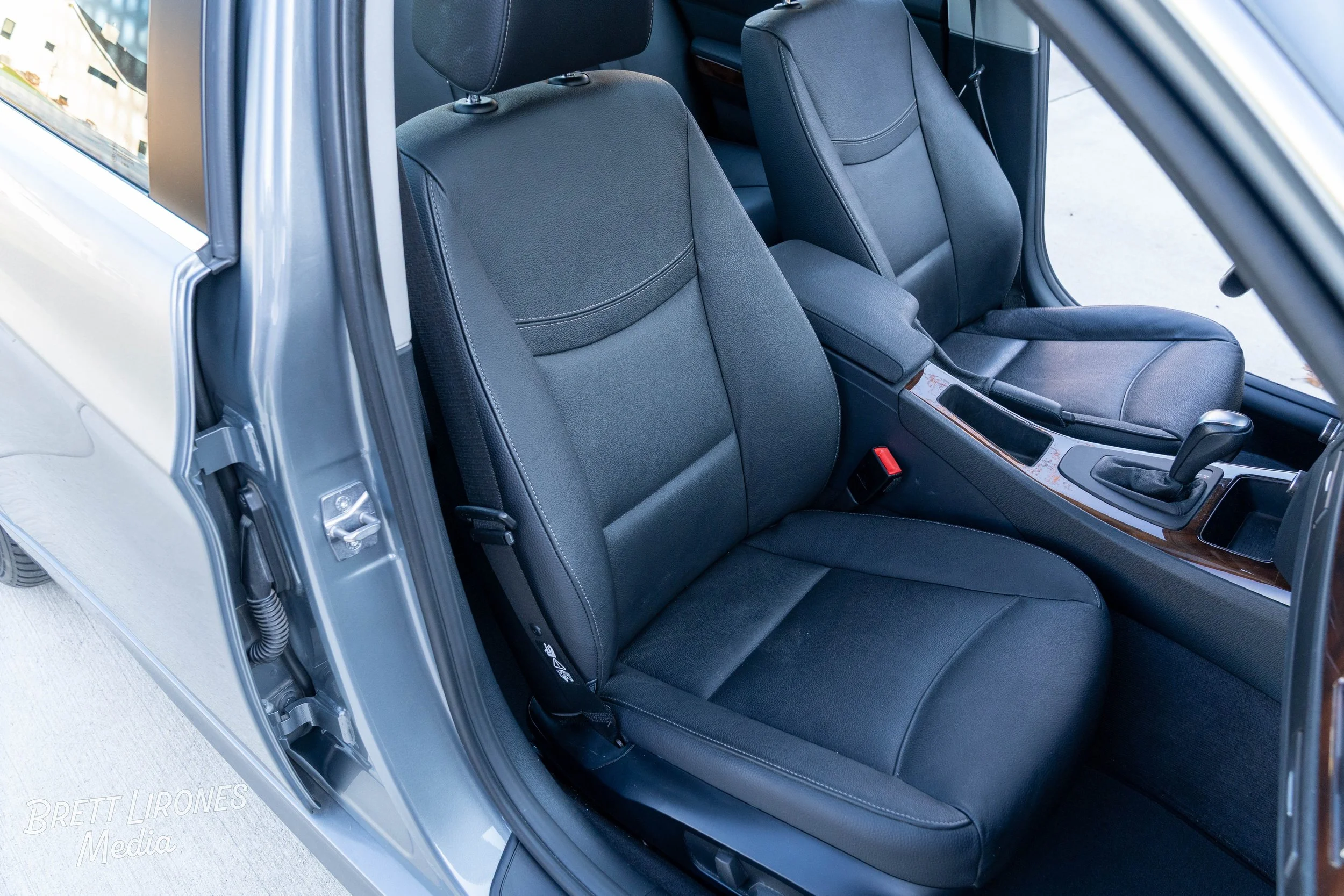 The image shows the interior of a car, focusing on the front passenger and driver seats which are covered in black leather. The center console, gear shift, and part of the dashboard are also visible, with a wood trim accent.