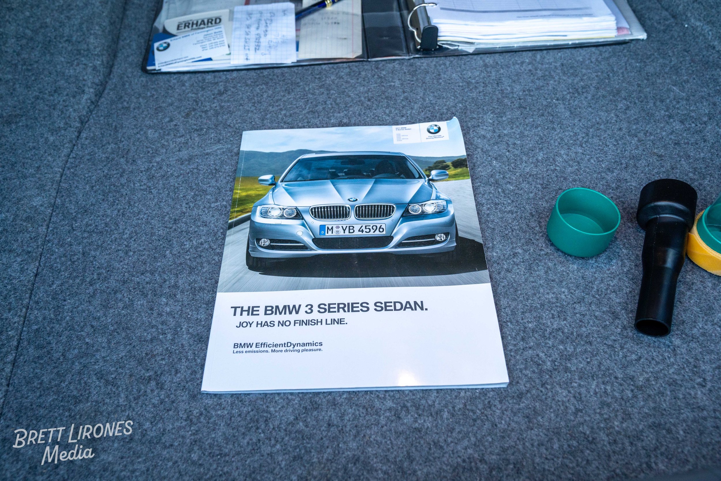 A magazine featuring a silver BMW 3 Series Sedan on a road with green landscape in the background. The magazine has text that reads: 'The BMW 3 Series Sedan. Joy has no finish line. BMW EfficientDynamics. Less emissions. More driving pleasure.' The m