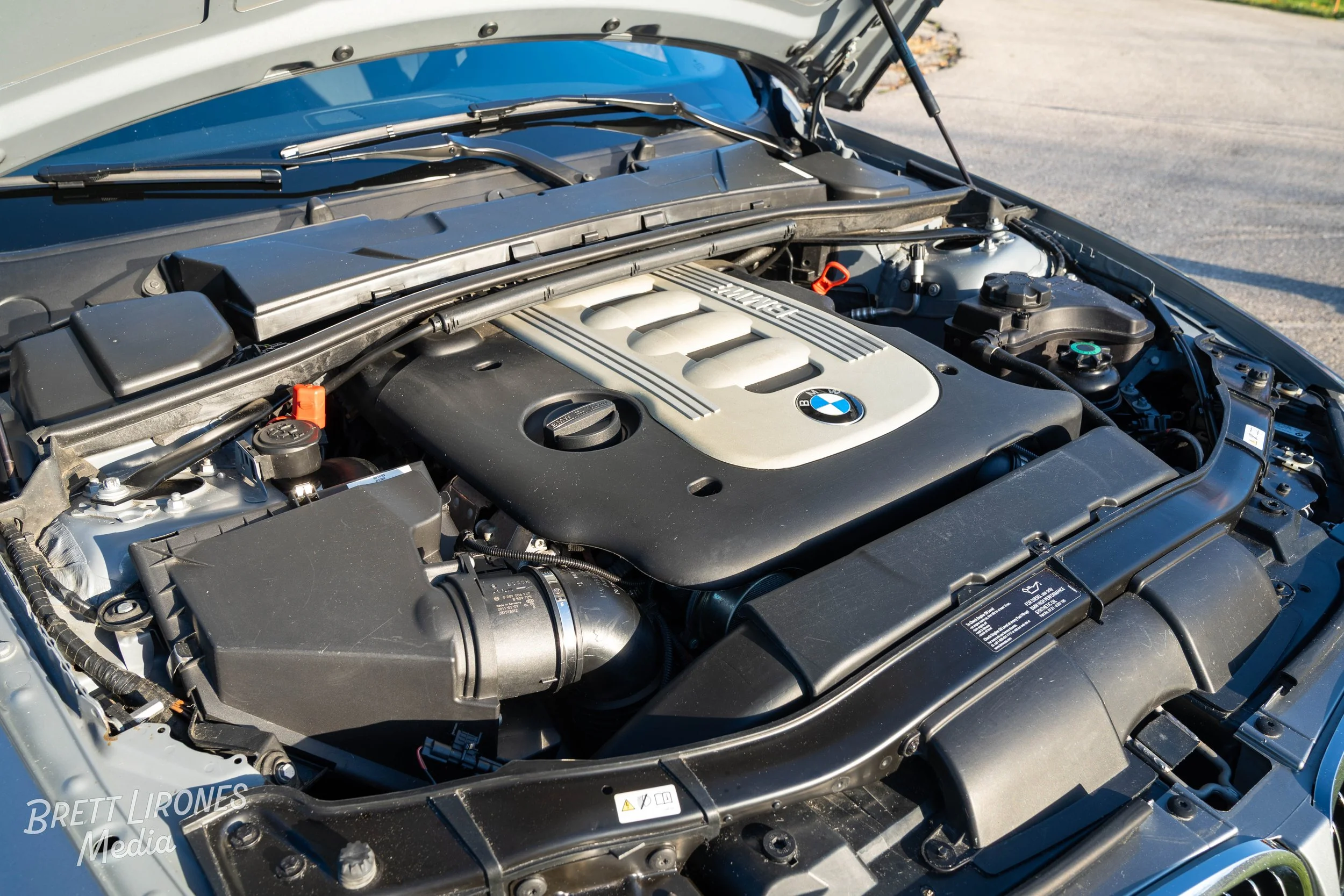Close-up view of a BMW engine bay with a silver engine cover and black surrounding components, open hood visible.