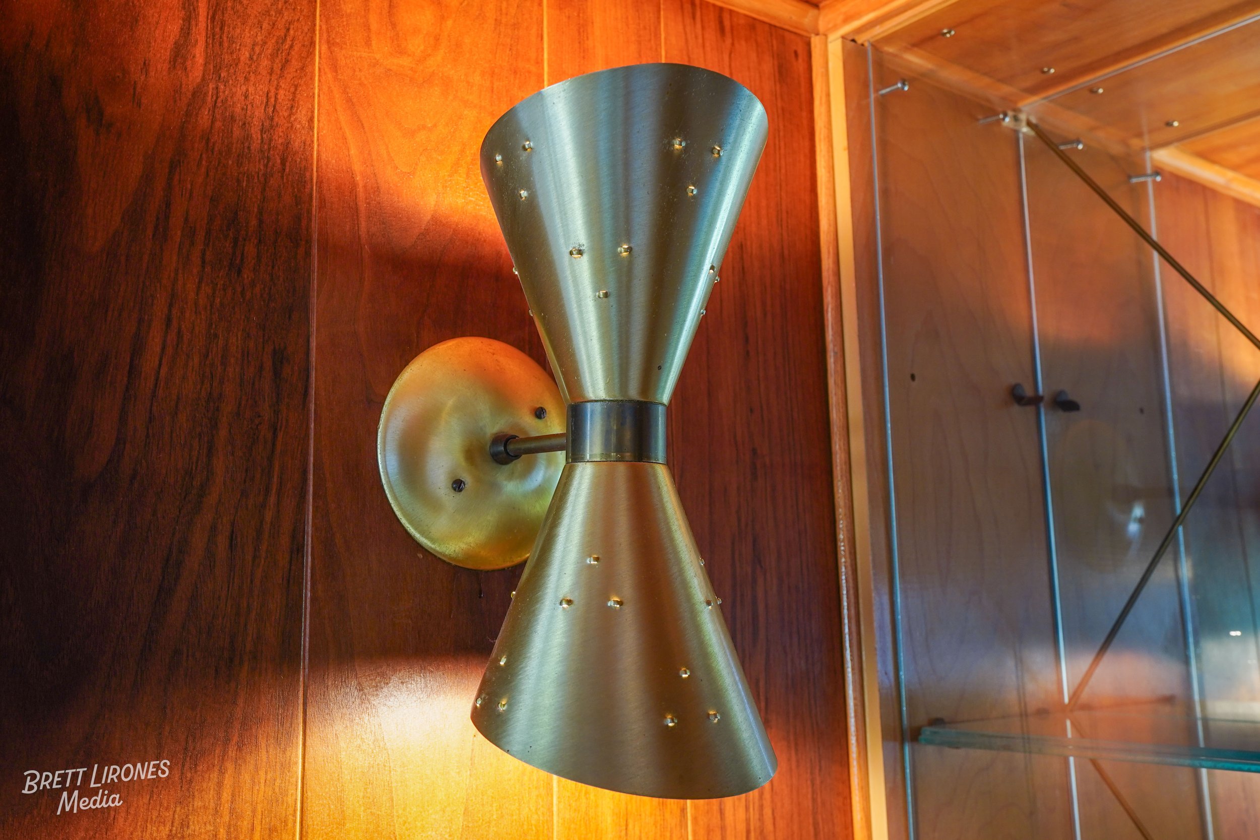 A modern, metallic wall sconce with a conical shape, mounted on a wooden wall.
