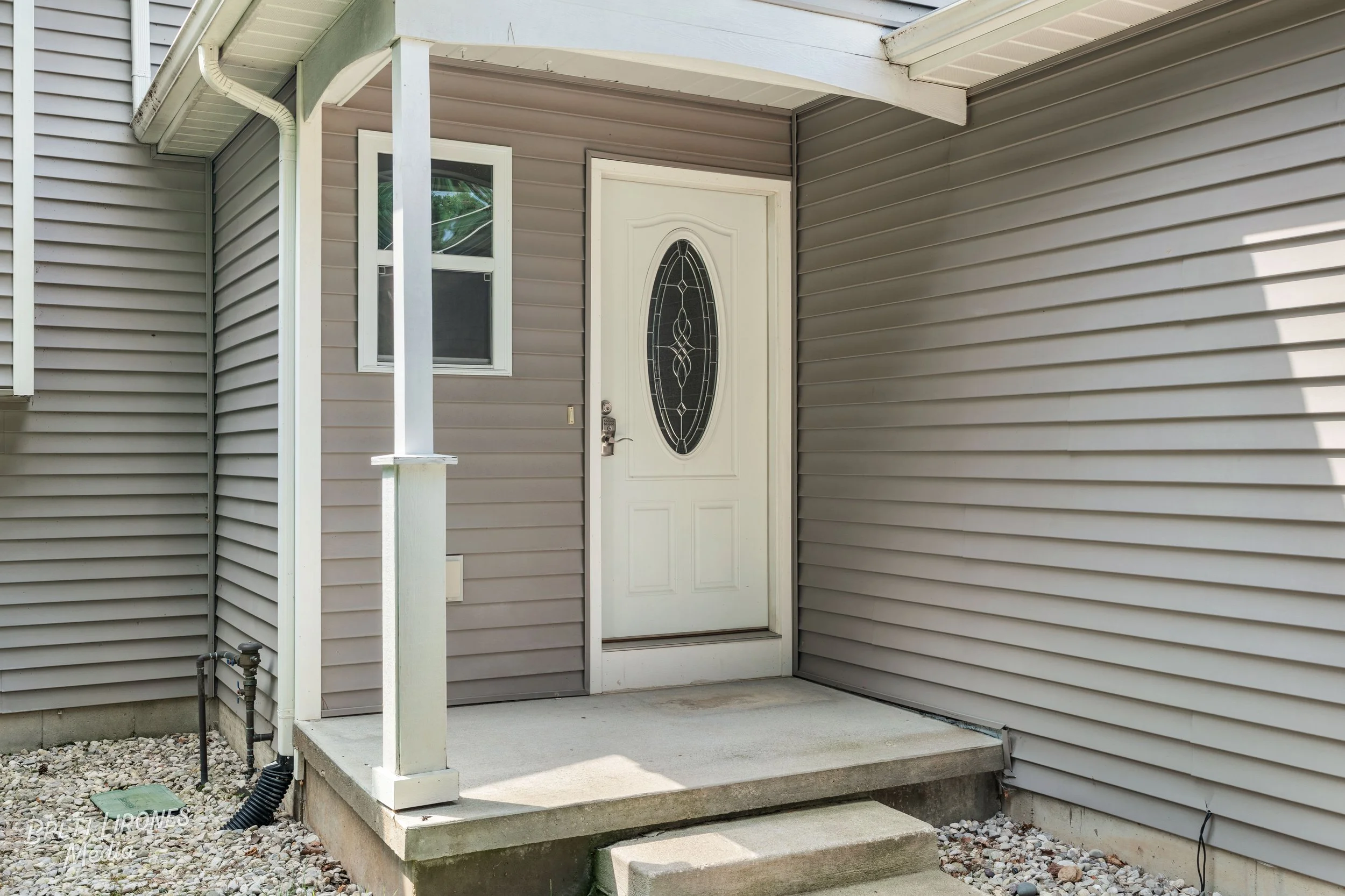 Front door of a house with a small porch, vinyl siding, a window to the left of the door, and a concrete step leading to the porch.
