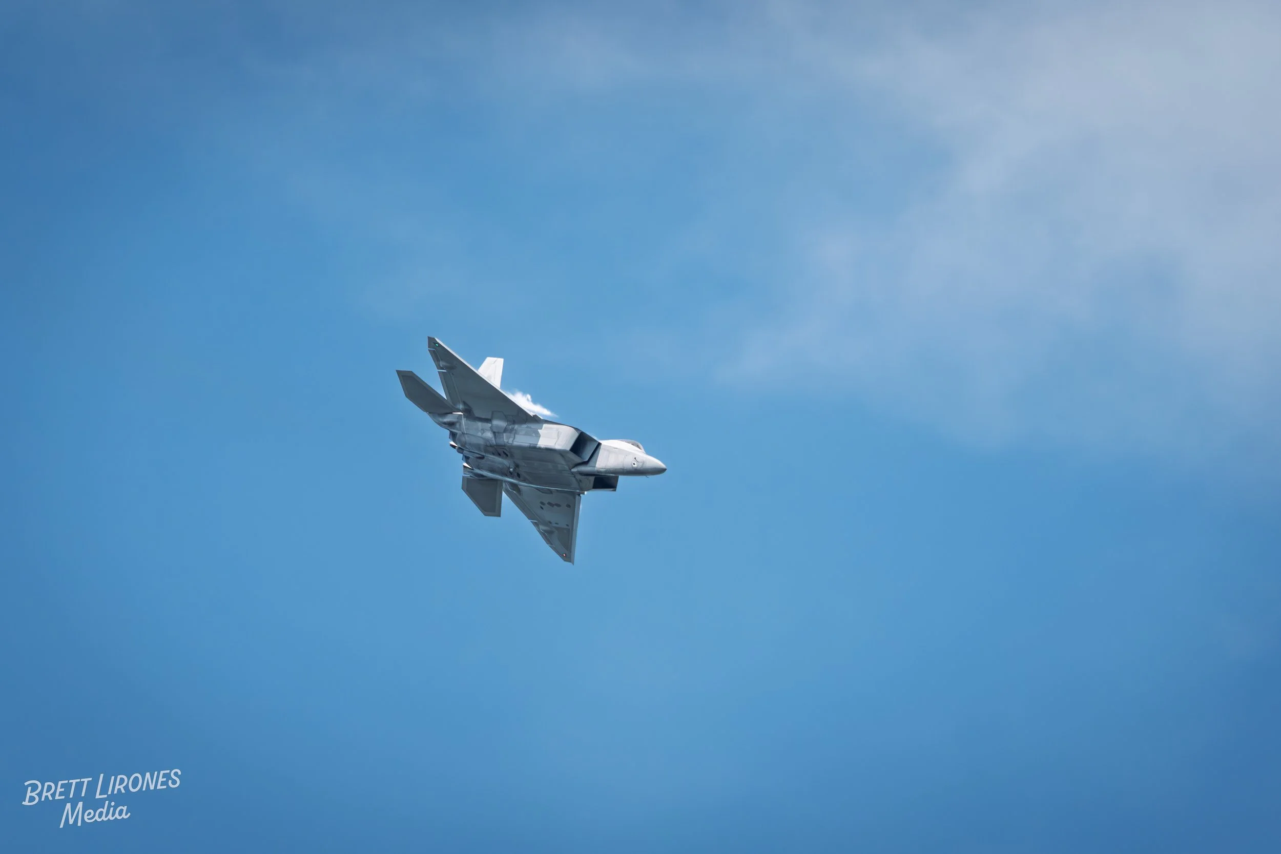 A fighter jet flying at high speed through a blue sky with wispy clouds.