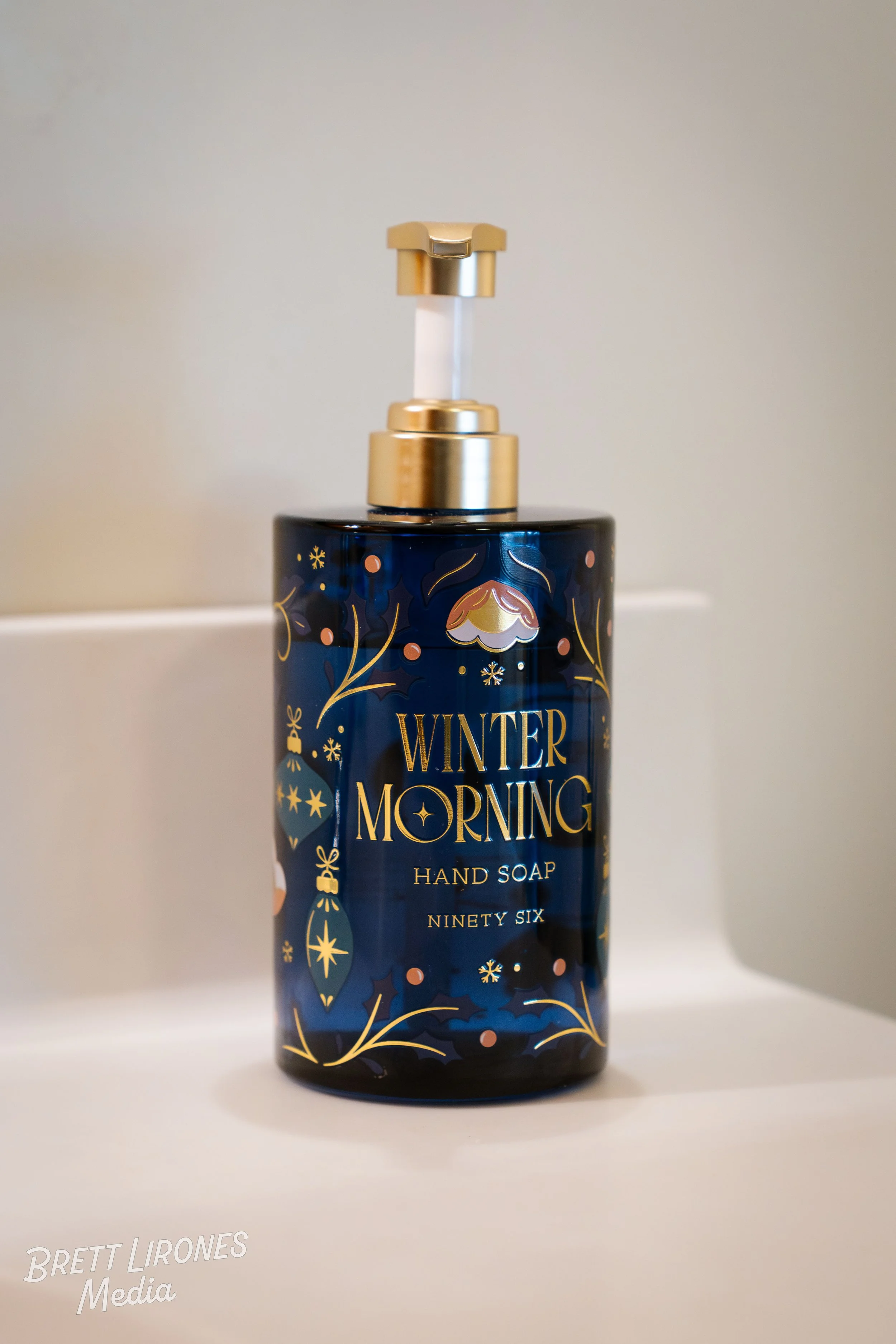 A bottle of hand soap with a dark blue, holiday-themed design labeled "Winter Morning" including Christmas ornaments, snowflakes, and decorative patterns.