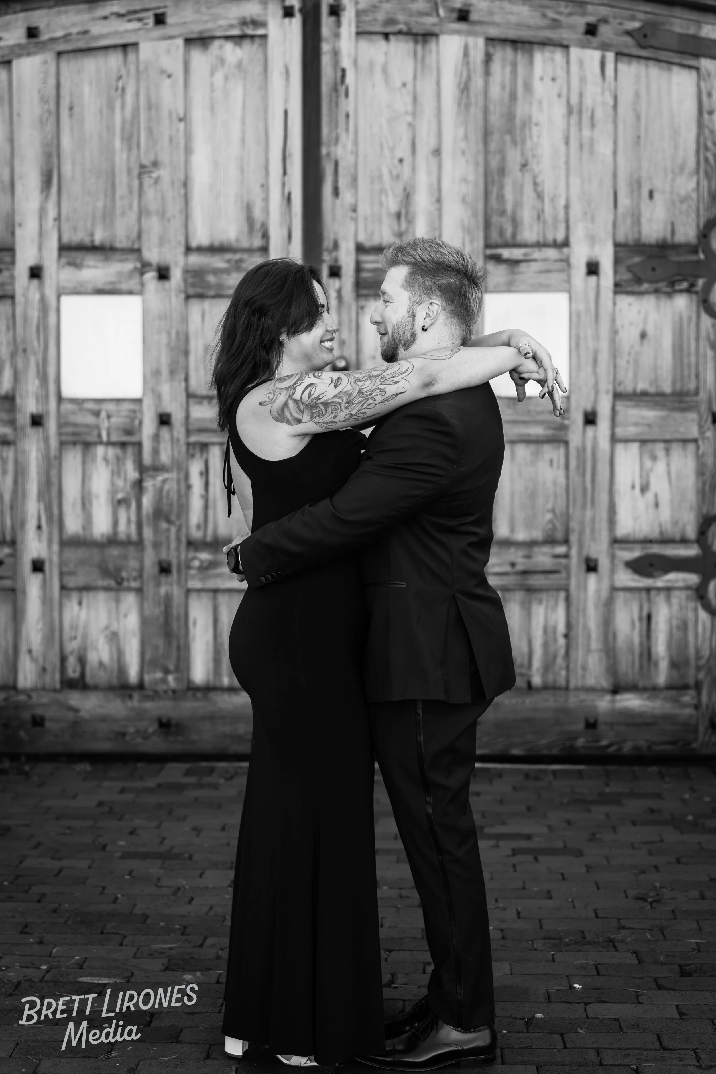 A couple dancing closely in front of a wooden barn door, smiling and embracing.