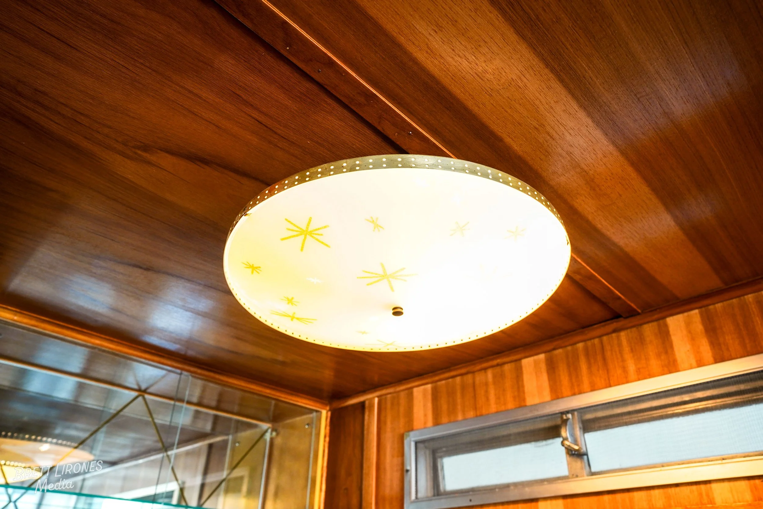 Decorative ceiling light fixture with star patterns, installed on a wooden ceiling with a wooden wall and window below.
