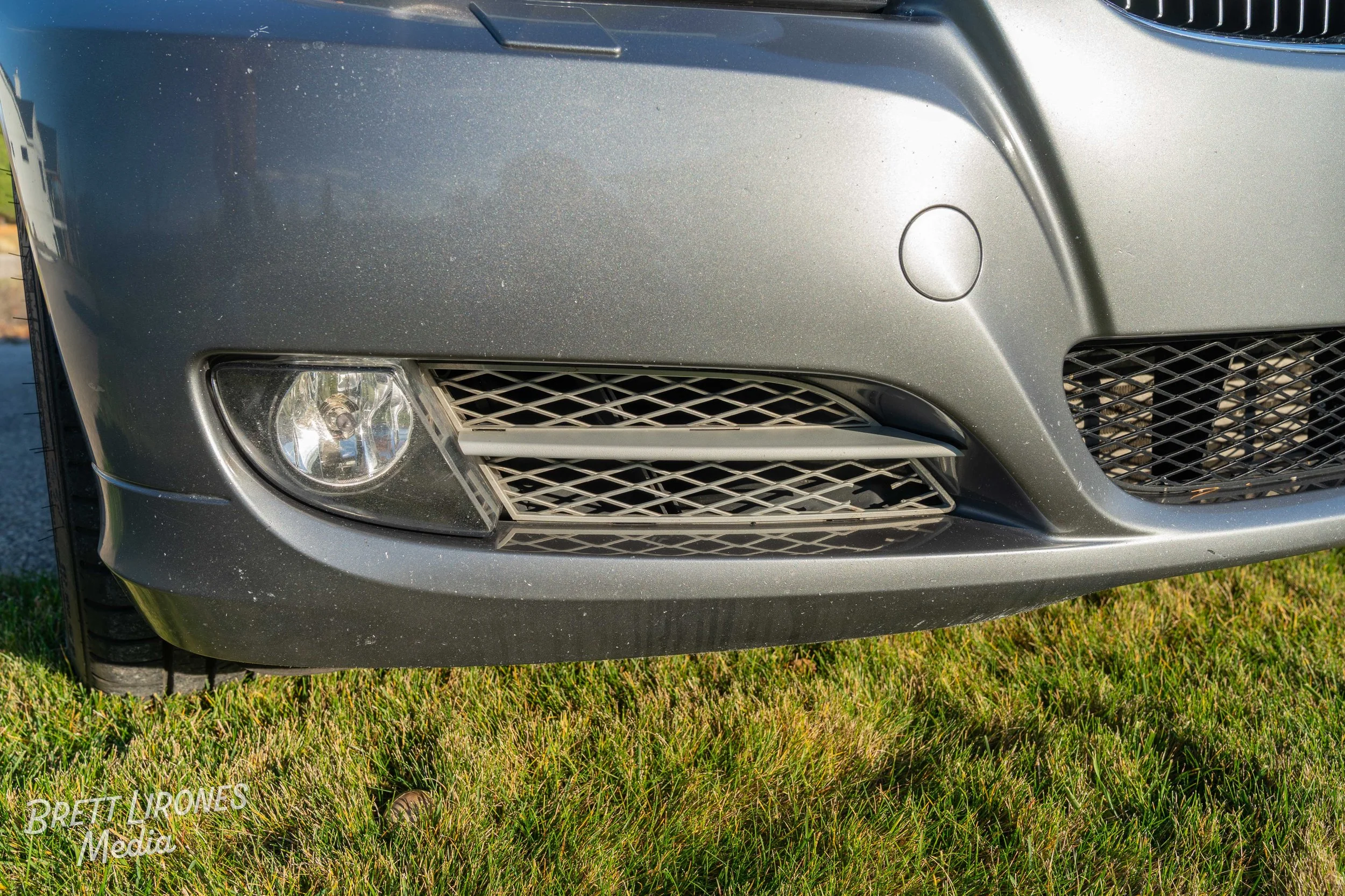 Close-up of the front bumper and headlight of a silver car parked on grass.