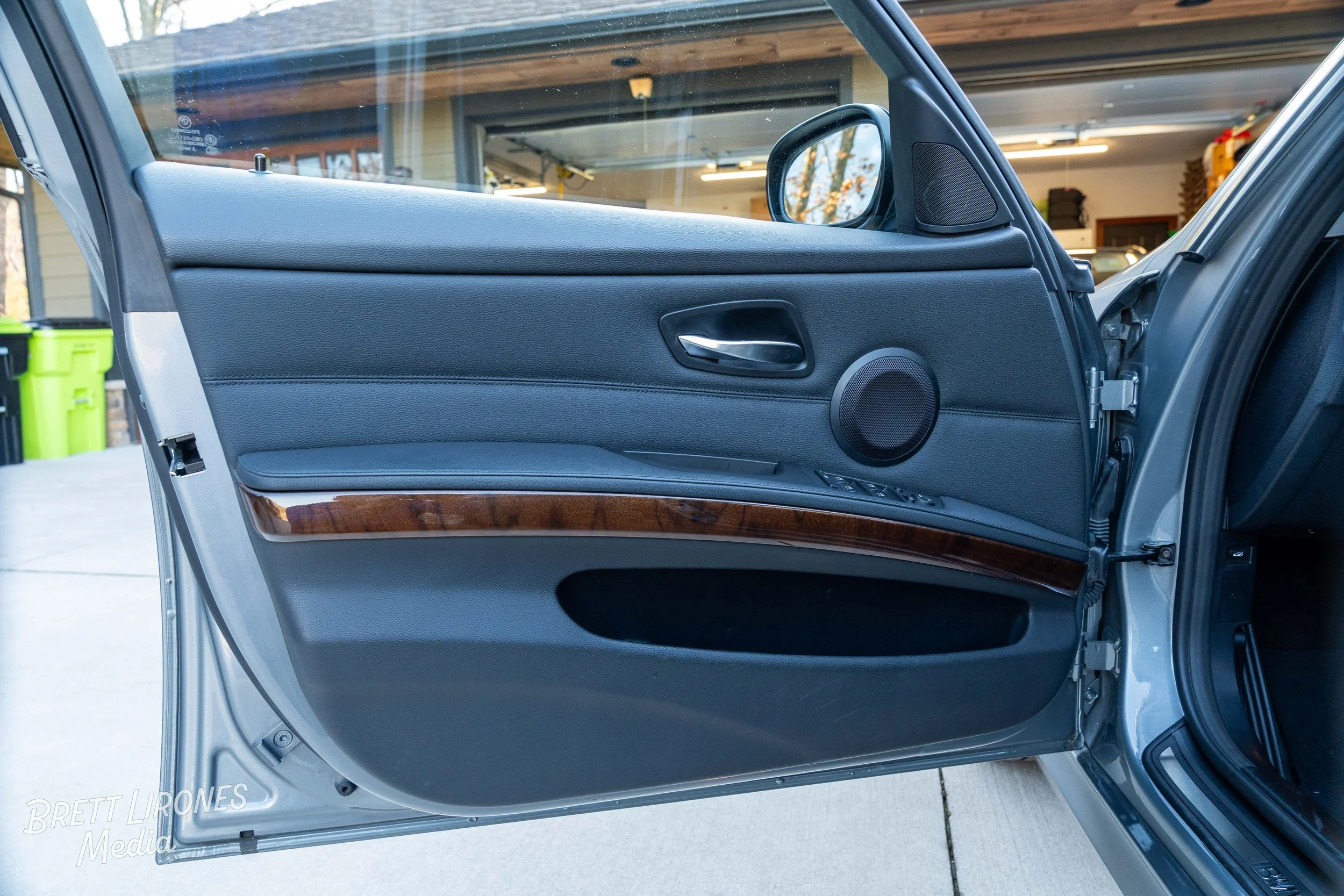 Interior of a car's front passenger door panel, showing the door handle, speaker, window controls, and a woodgrain trim.