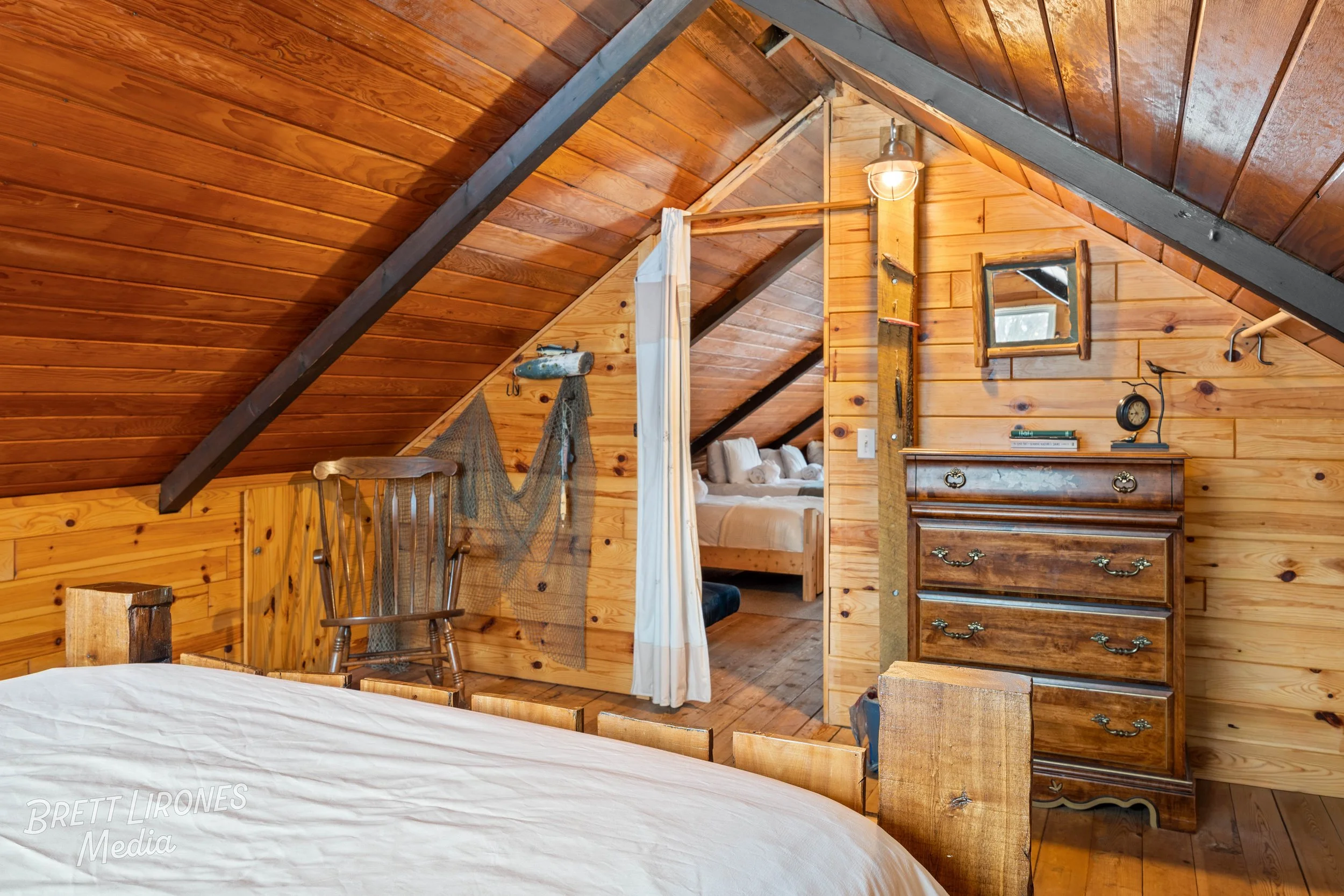 A cozy wooden attic bedroom with sloped ceilings, a bed, and vintage furniture.
