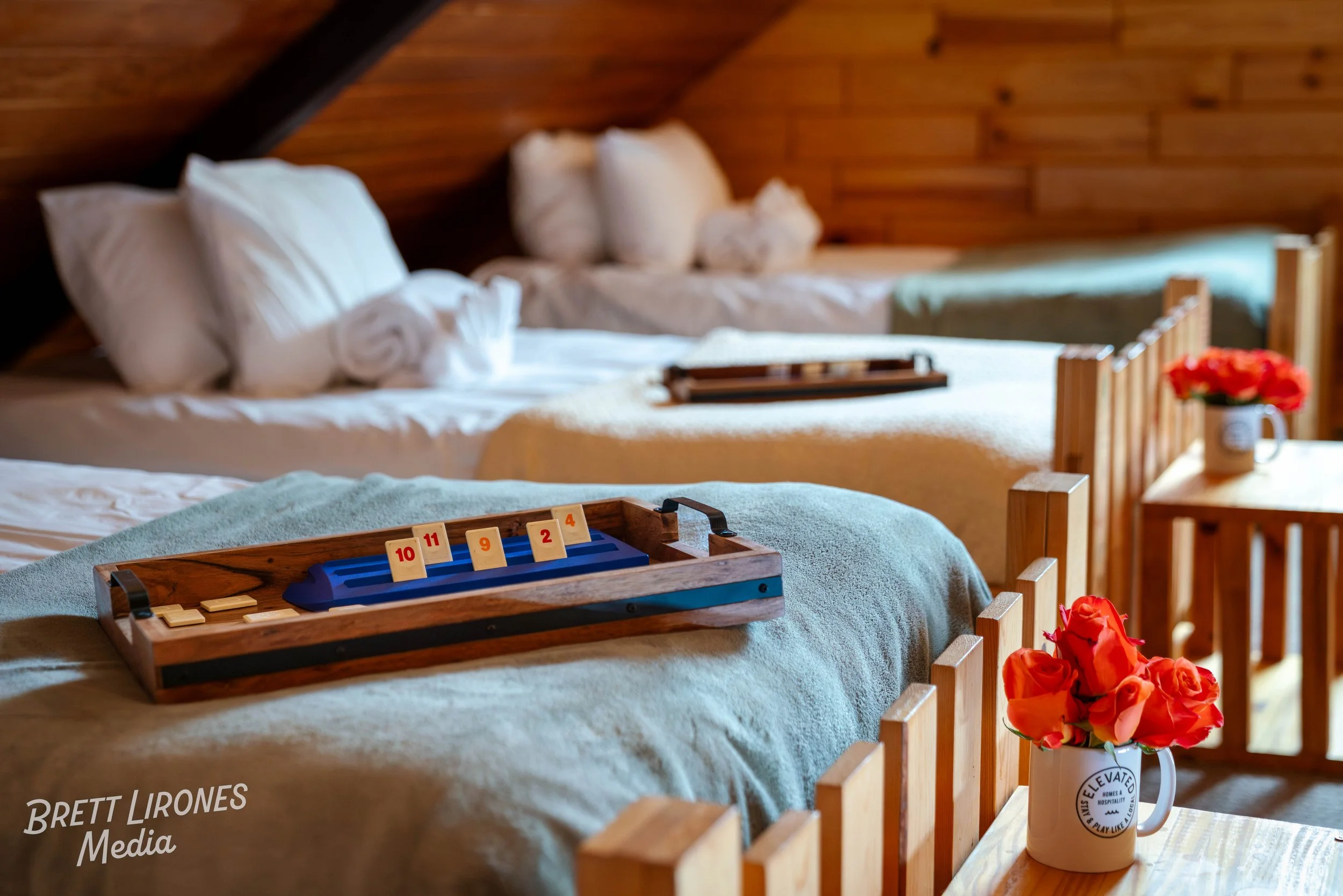 Three beds in a wood-paneled room with a tray of game pieces on the middle bed and a mug with orange flowers on a side table.