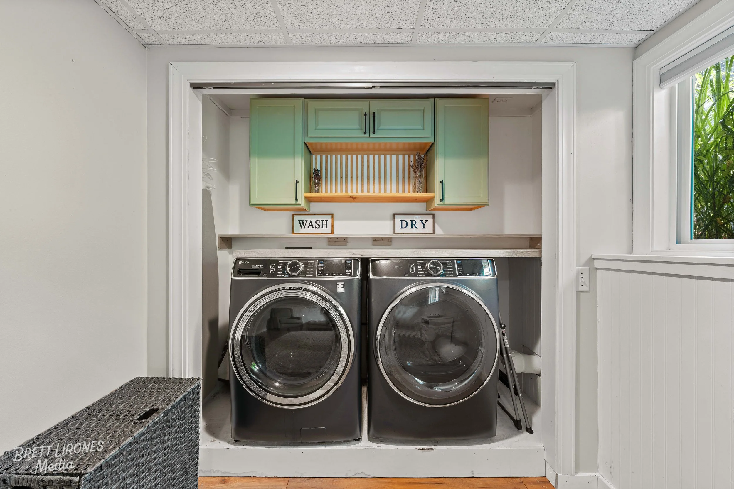 Laundry room with a front-loading washer and dryer, green cabinets, and signs labeled 'WASH' and 'DRY'.