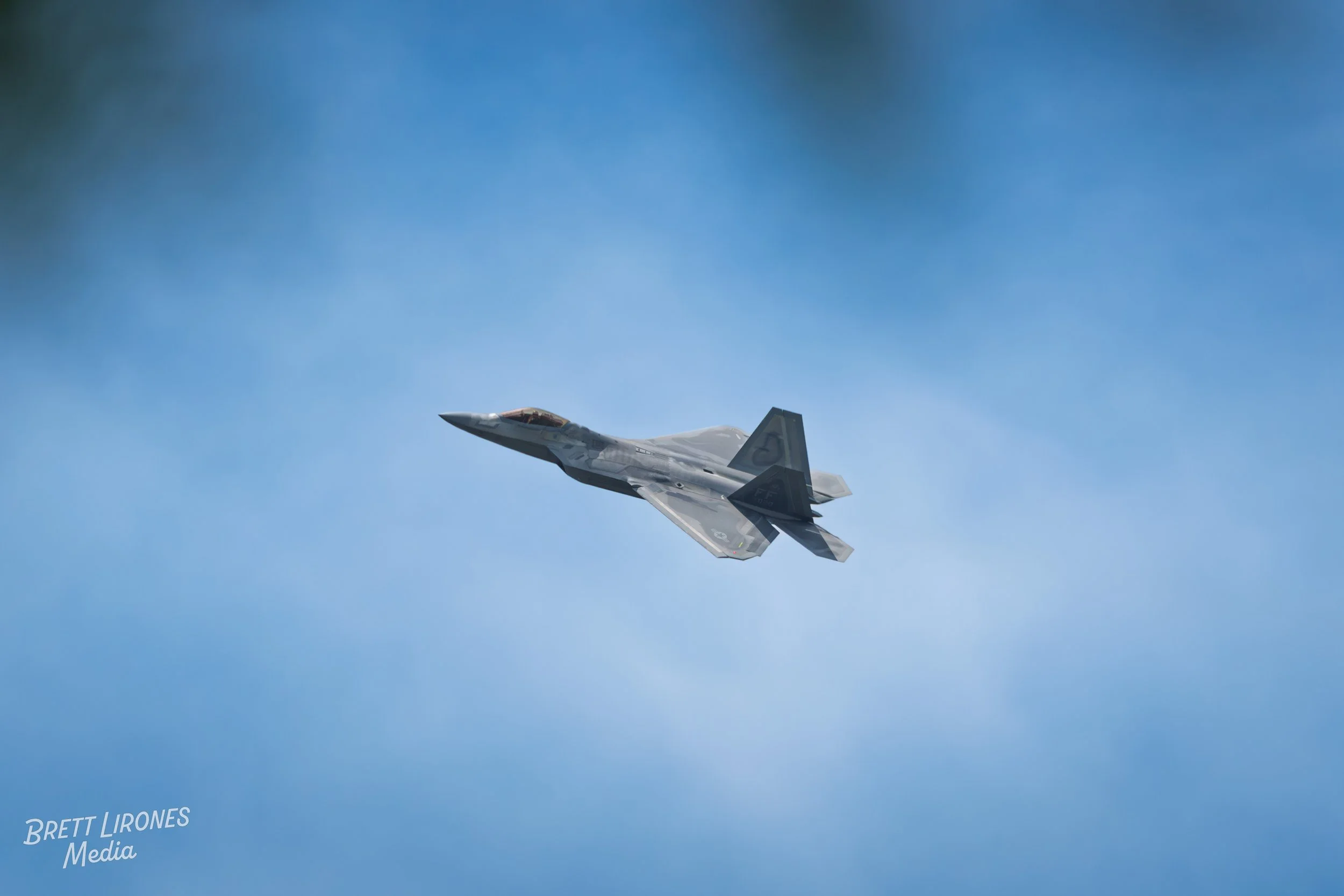 An F22 Raptor fighter jet flying through a clear blue sky.