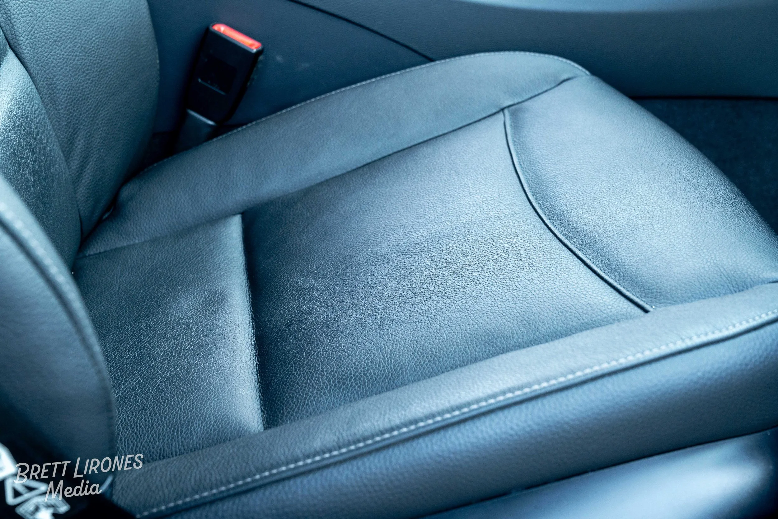 Close-up of a black leather car seat with visible stitching and a seatbelt buckle on the side.