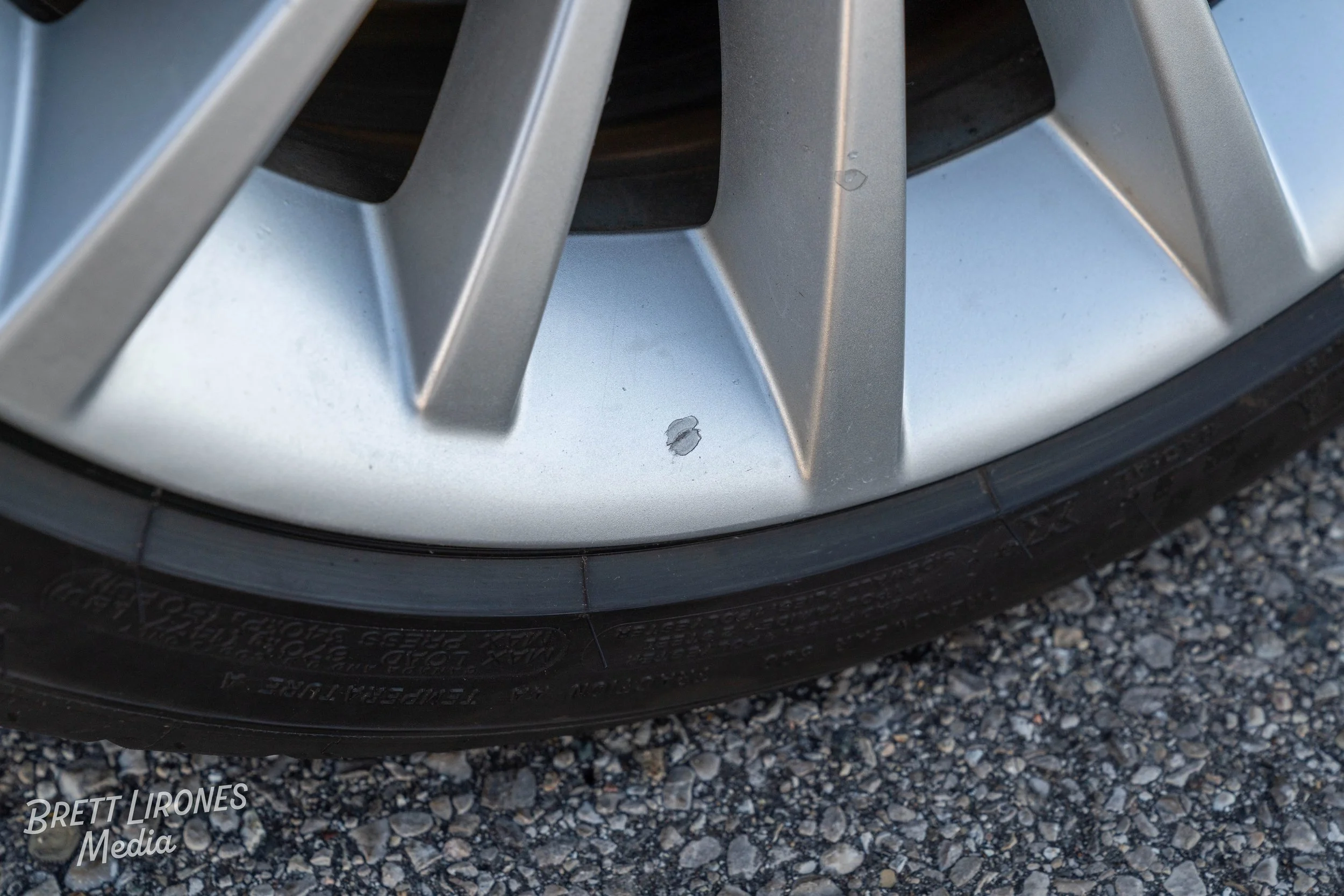 Close-up of a car wheel with a scuff mark on the silver rim, on a gravel surface.