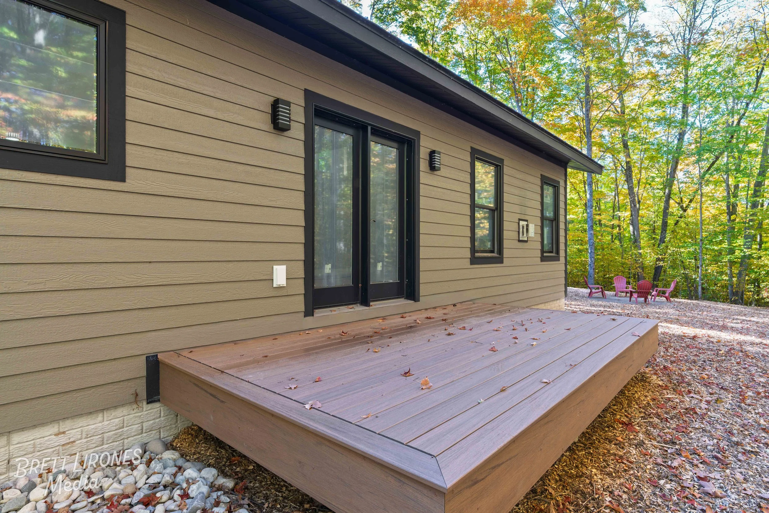 Backyard with a small wooden deck attached to a house, surrounded by trees with fall foliage, and pink chairs arranged in a circle in the distance.