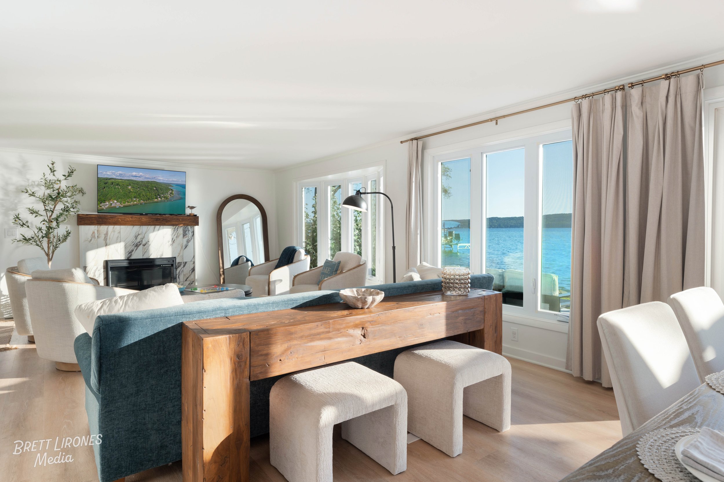 Living room with large windows overlooking a lake, with chairs, a fireplace, and decor.