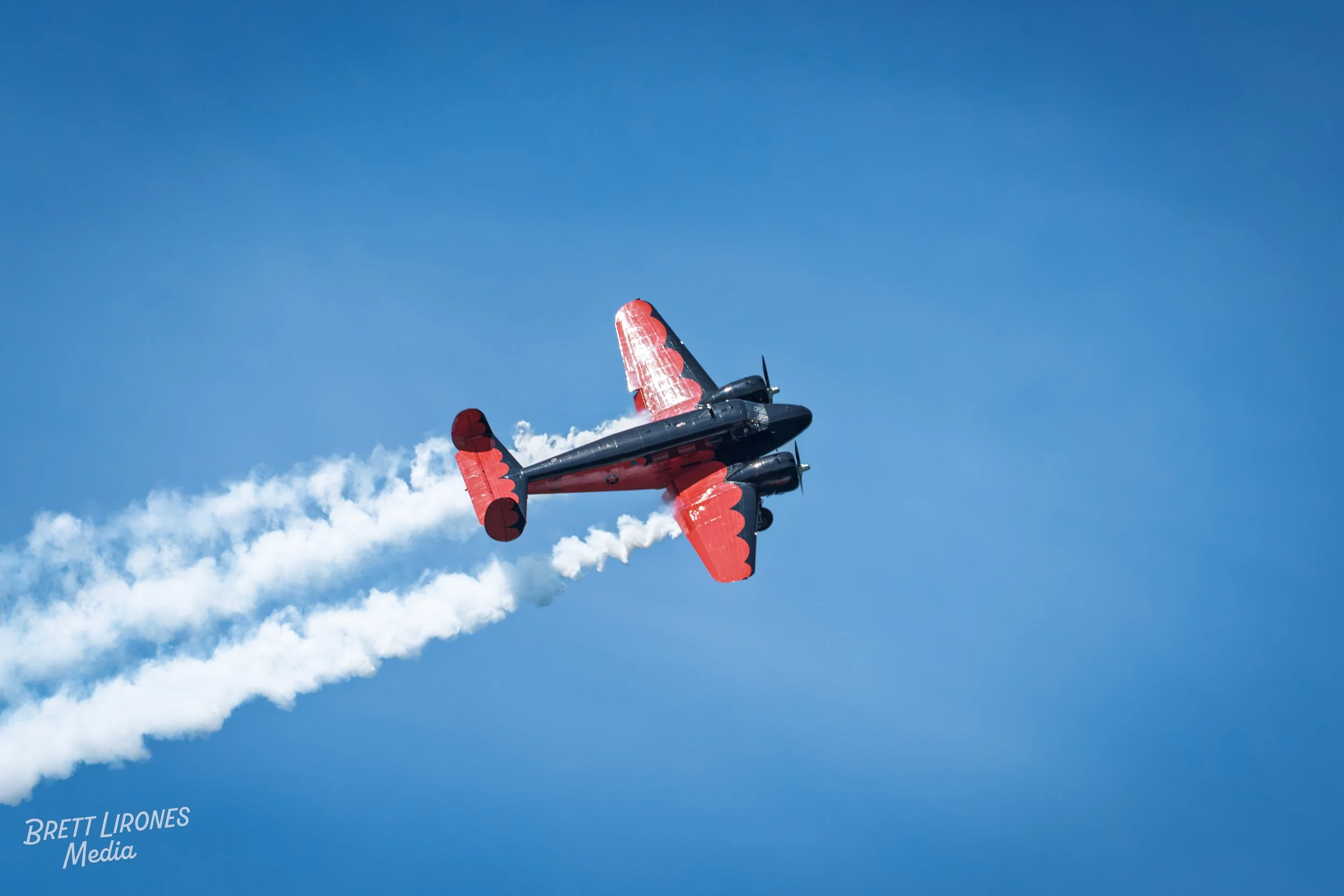 An airplane flying through the blue sky, leaving white smoke trails behind.