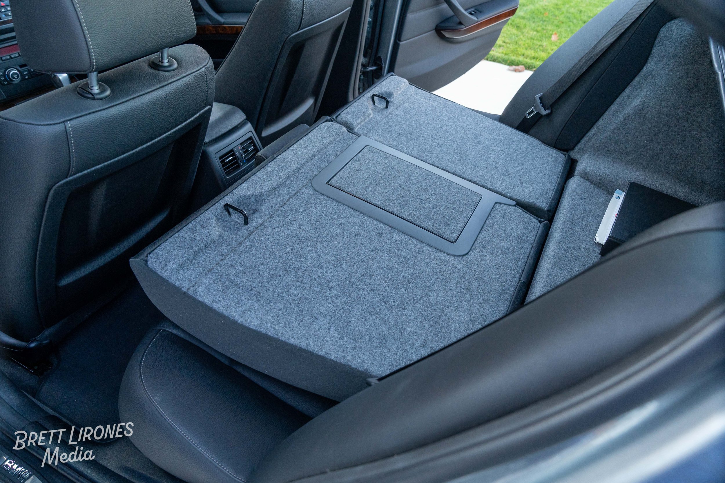 The rear seats of a car with one seat folded down, revealing a gray carpeted cargo area with a rectangular hatch or access panel.