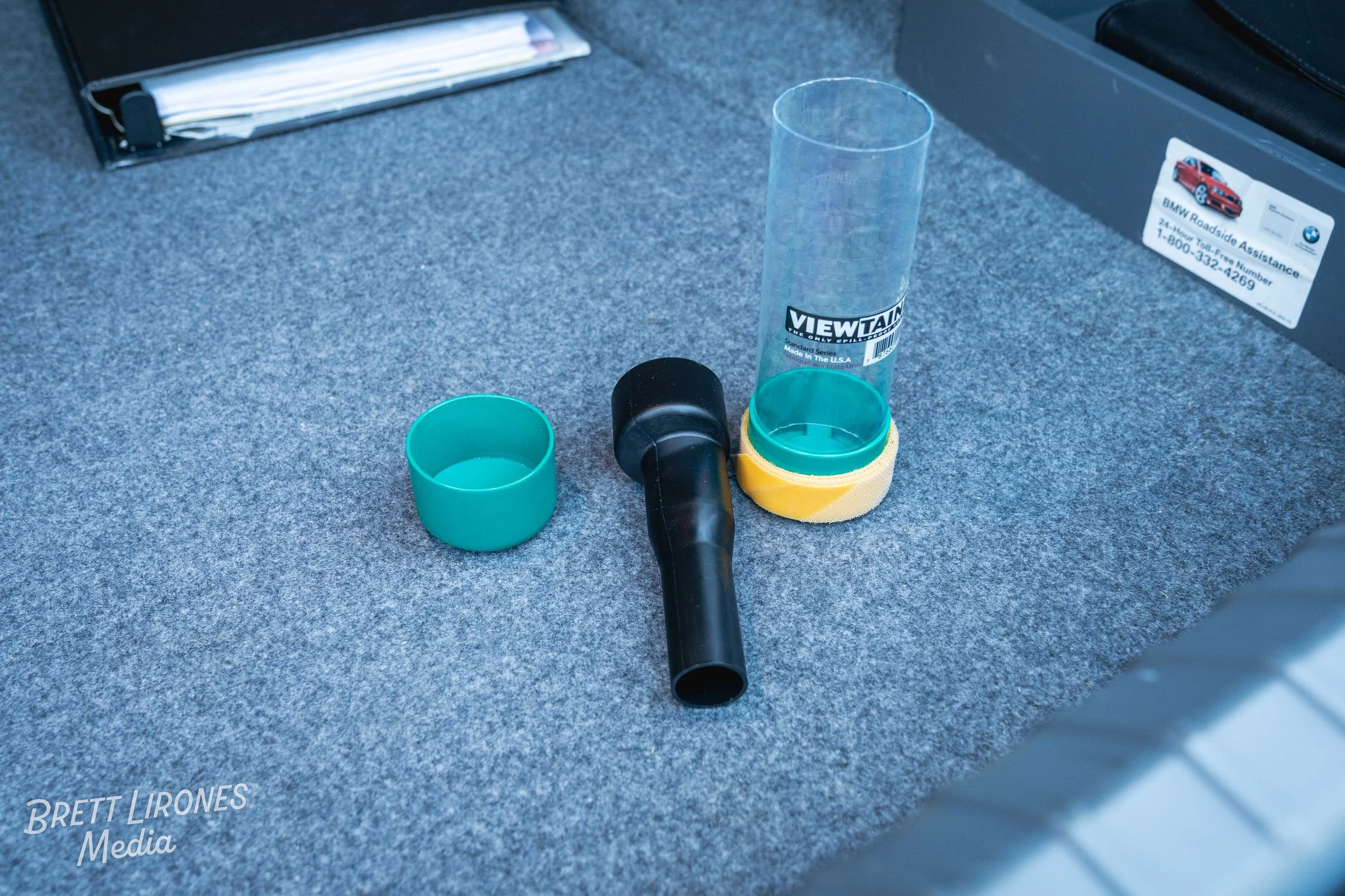 A black device with a long tube connected to a transparent cylindrical container and a green cap, all placed on a gray surface.