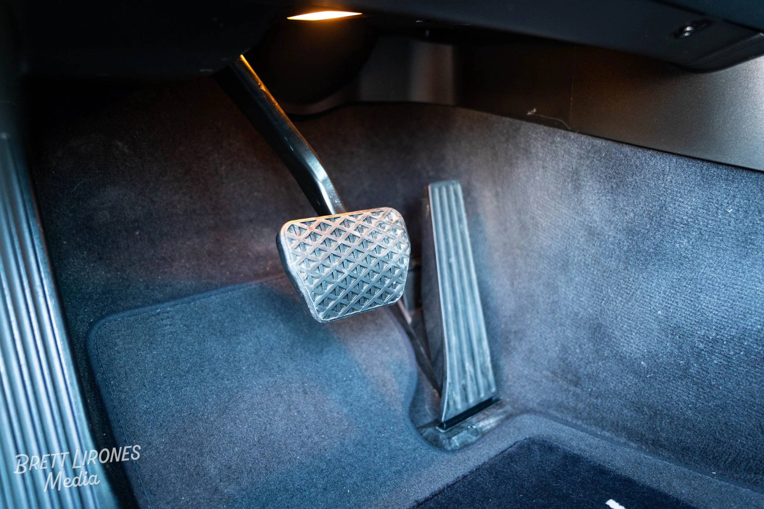 Close-up of a car's accelerator and brake pedals in a vehicle's footwell.