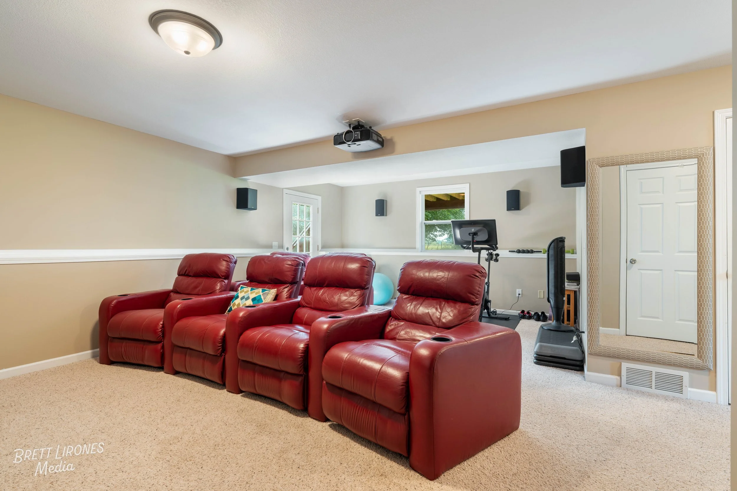 Home theater room with four red leather recliners, a mirror, and fitness equipment with a treadmill and a large mirror.