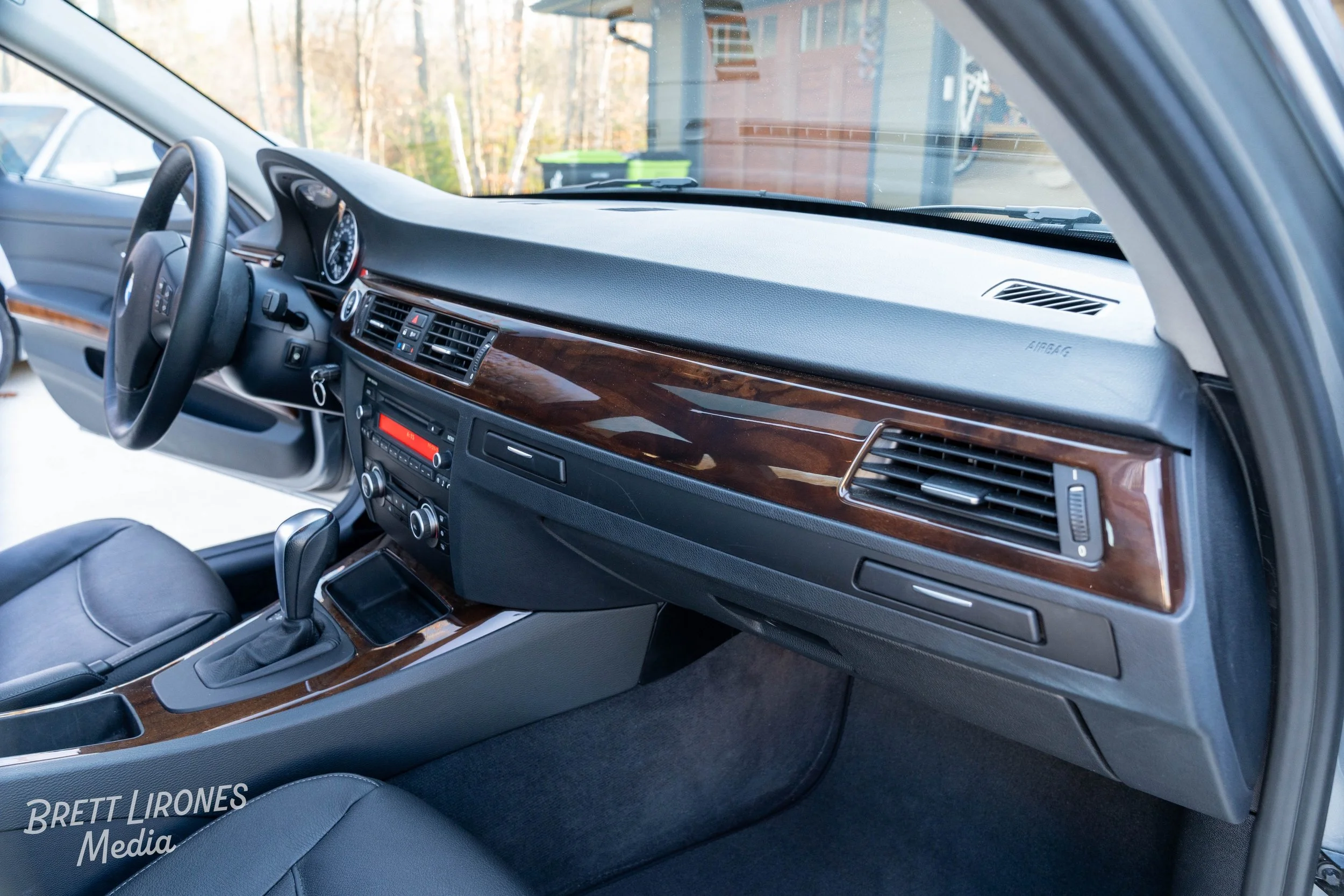 Inside view of a car's front interior showing the dashboard, steering wheel, gear shift, and center console with wood trim.