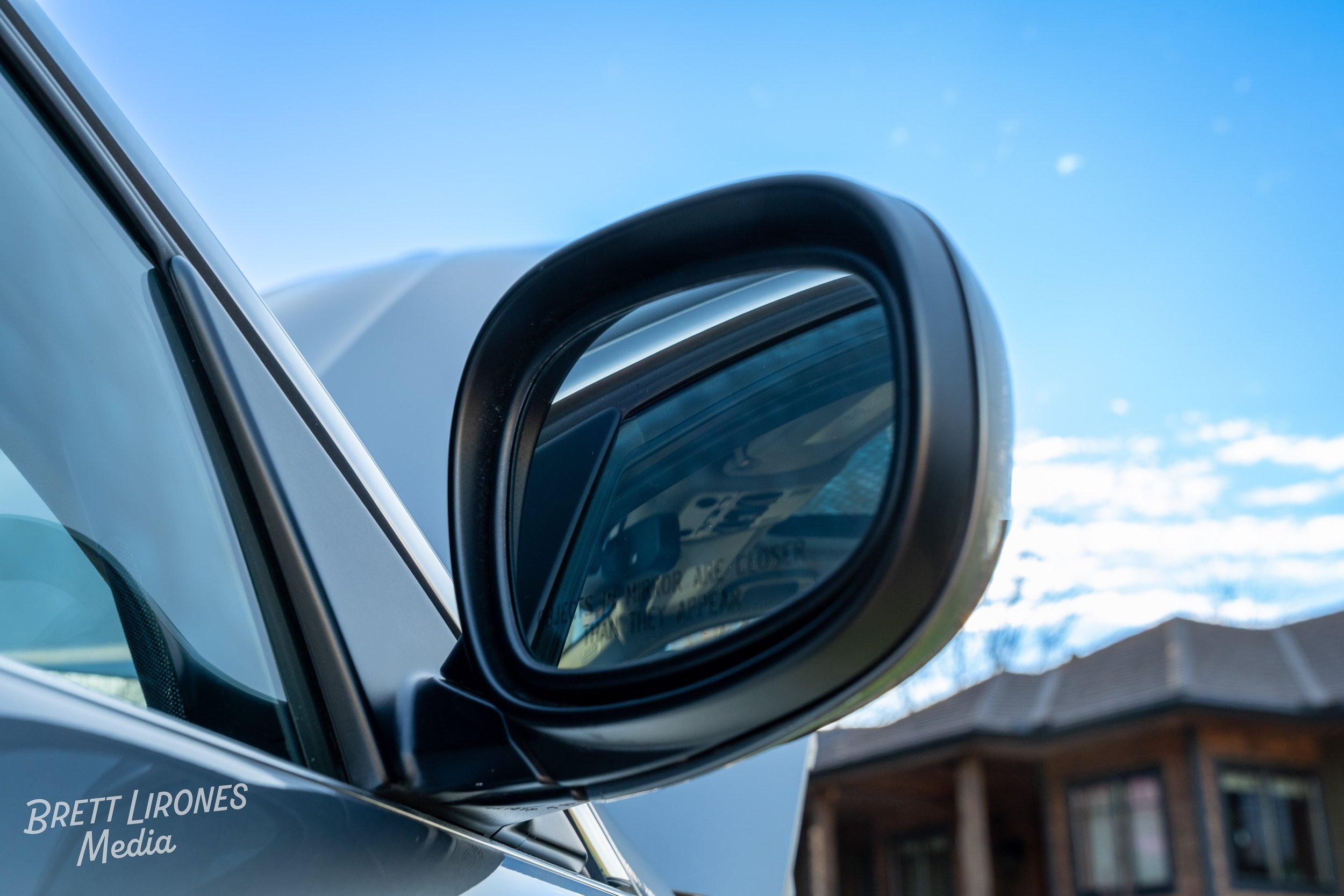 Close-up of a car's side mirror reflecting a building and blue sky.