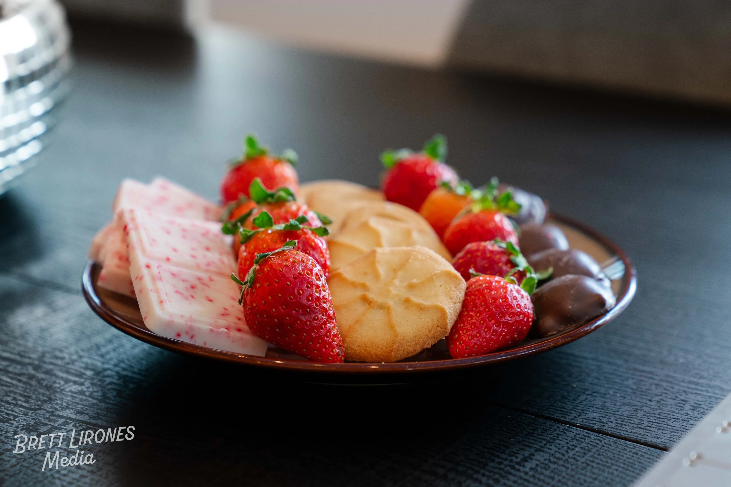 Plate of strawberries, sugar cookies, and chocolate-covered strawberries on a dark wooden table.