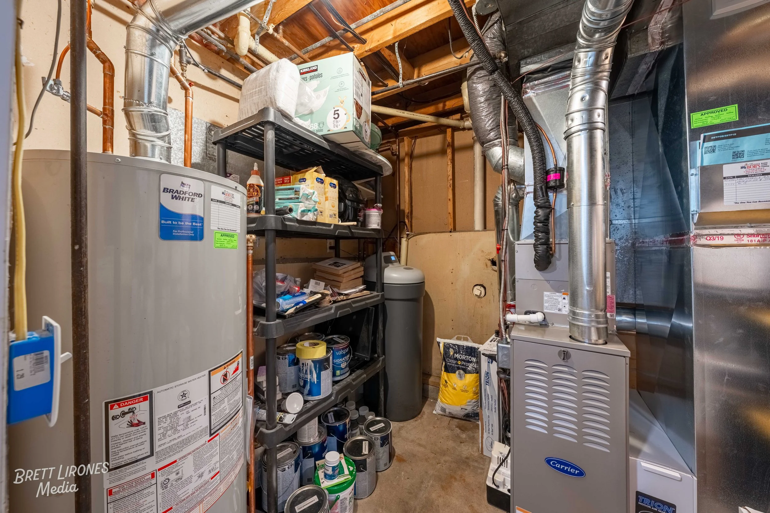 An organized utility room with a water heater, storage shelves filled with household supplies, and an HVAC system with ductwork.